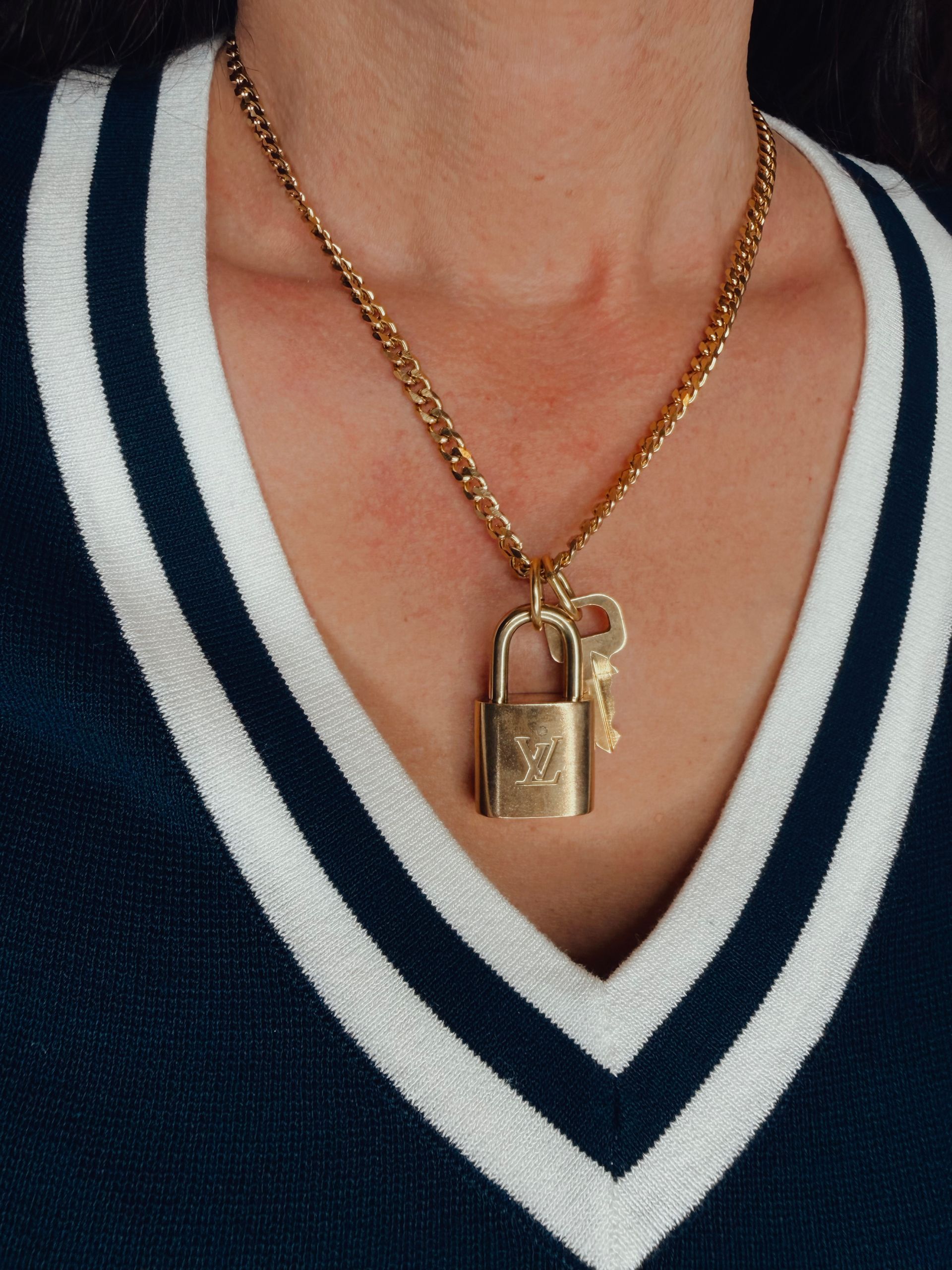 Gold padlock pendant on a chain over a navy-and-white V-neck sweater