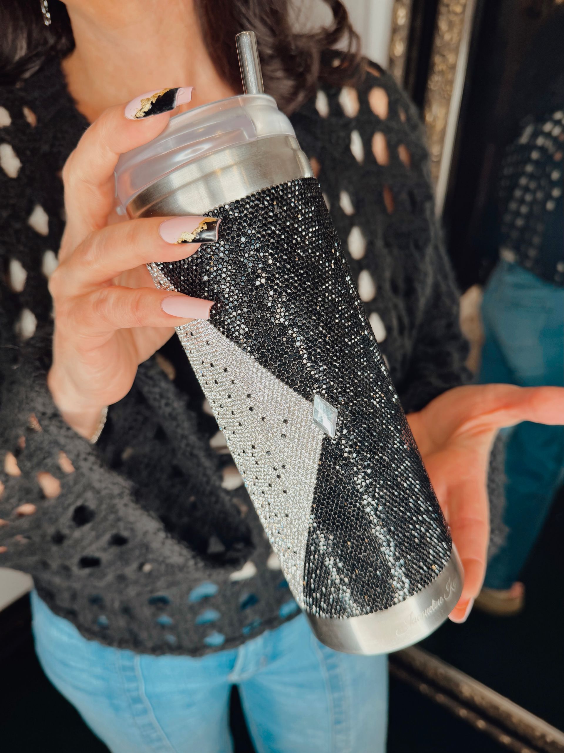 Person holding a black-and-silver glitter tumbler with a clear lid and straw