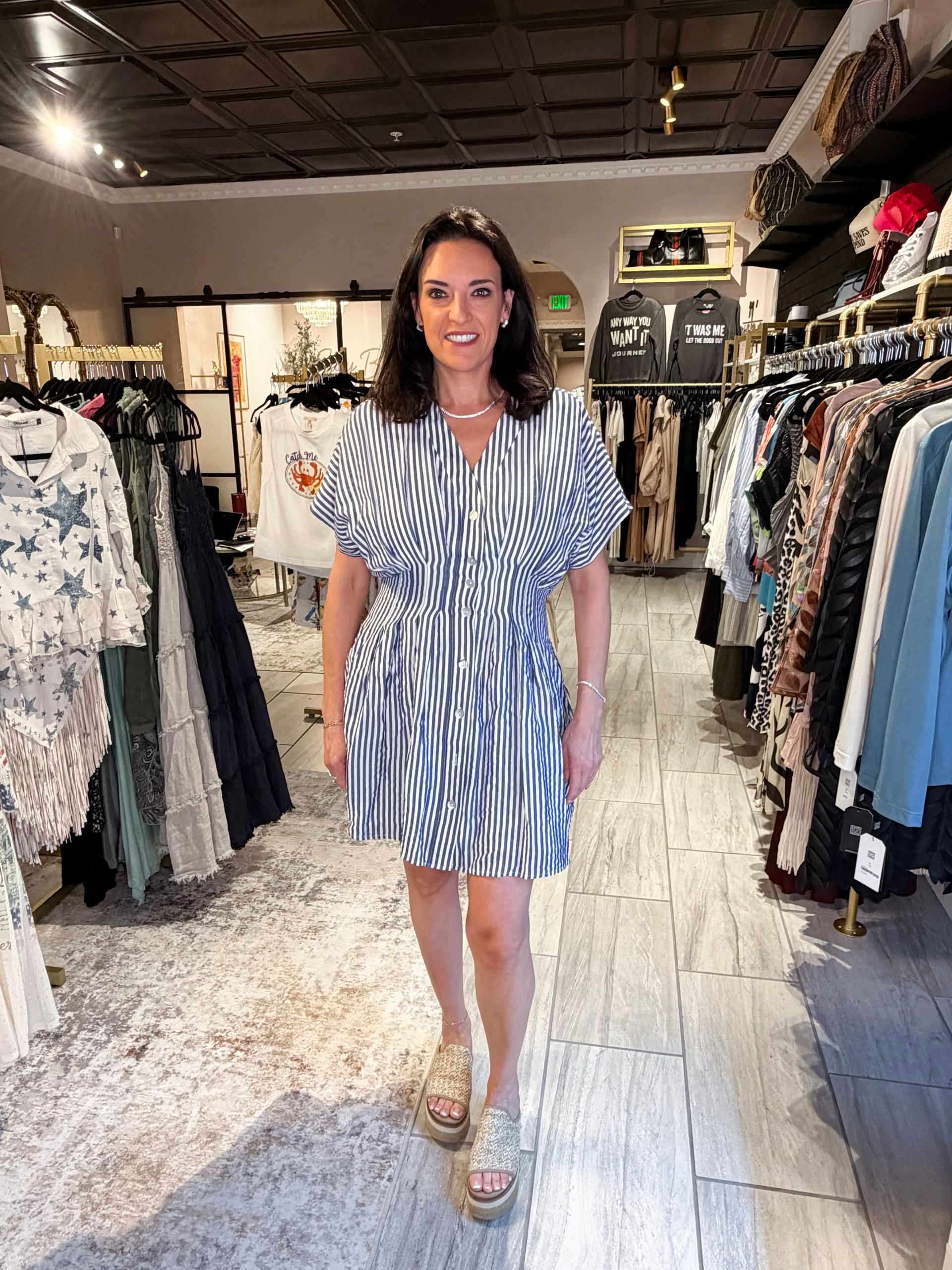 Woman in blue-and-white striped dress standing in a boutique clothing store aisle