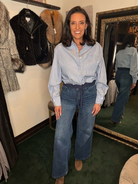 Woman in a blue striped shirt and jeans standing in a boutique fitting room.