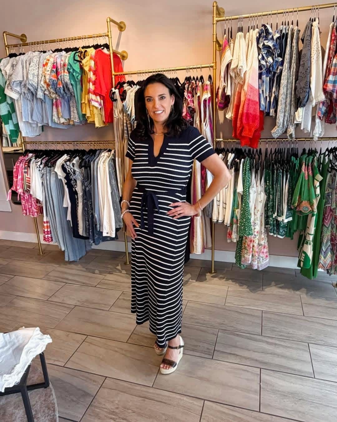 Woman in a striped black dress posing in a clothing boutique with racks of colorful garments.