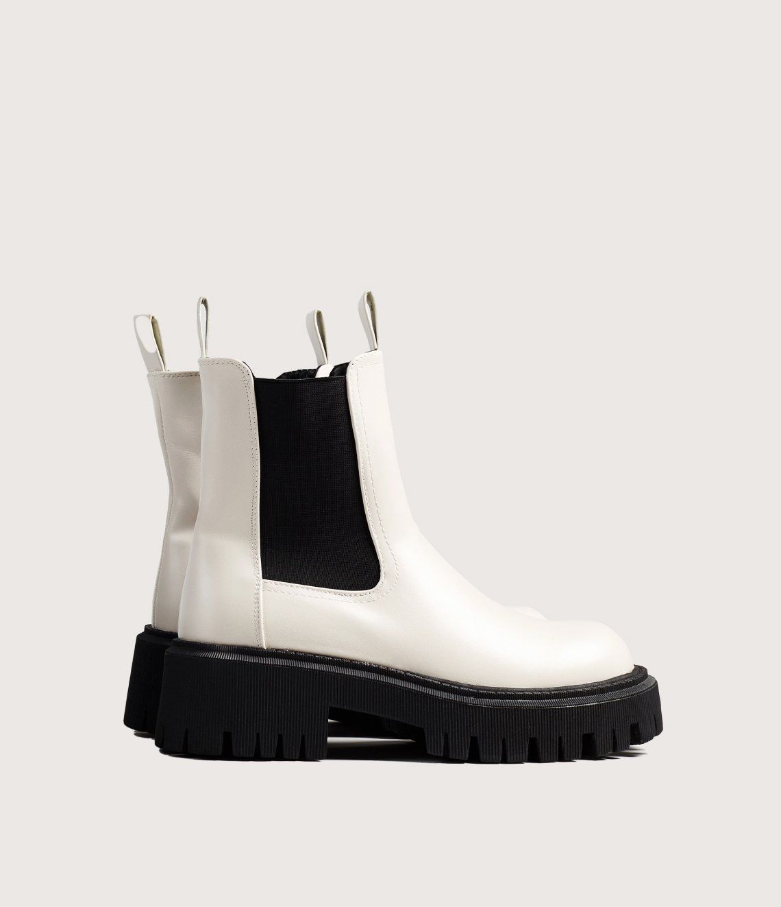 A pair of white chelsea boots with a black sole on a white background.