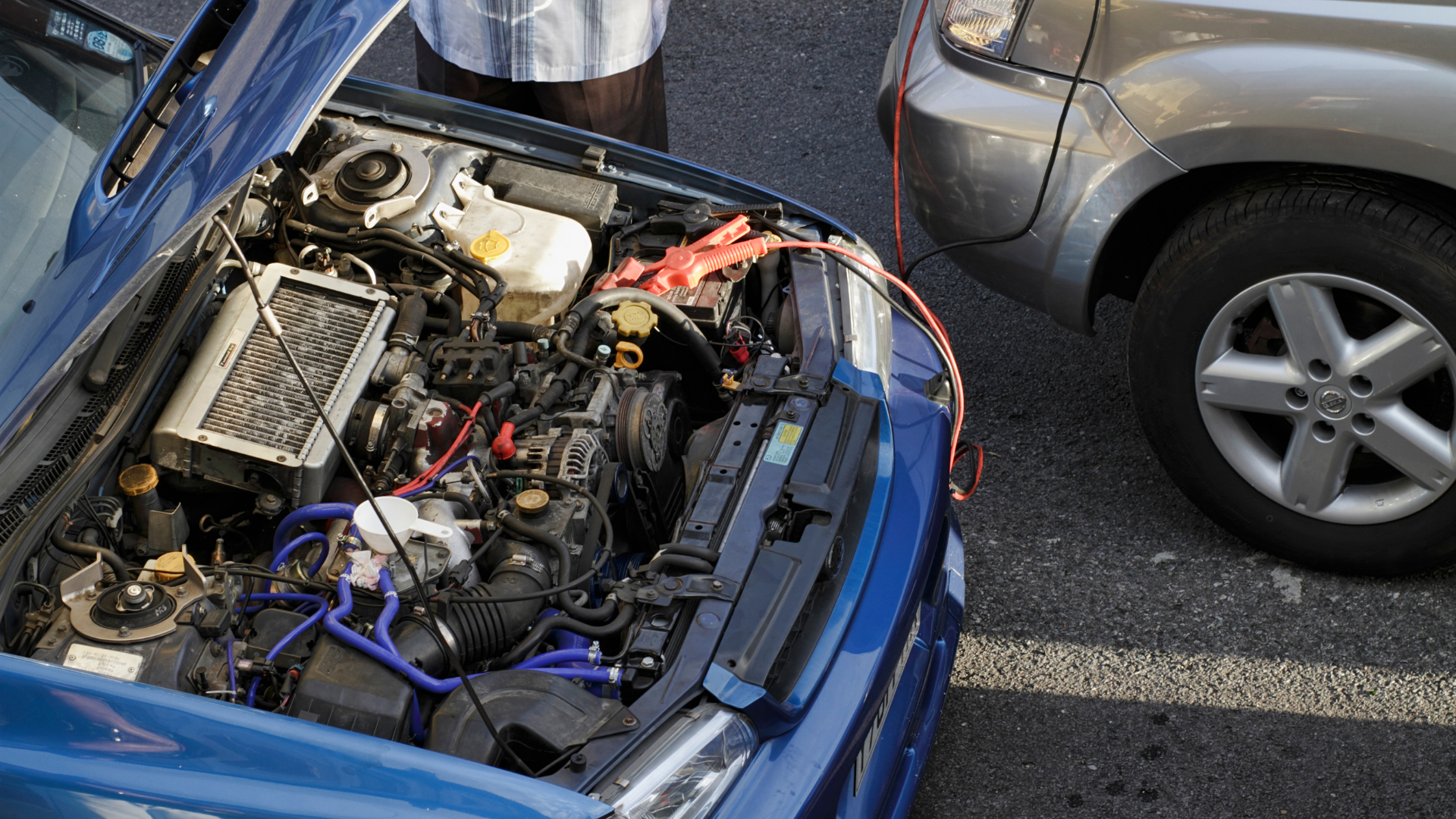 Blue car with open hood showing engine bay in a parking lot beside a gray car