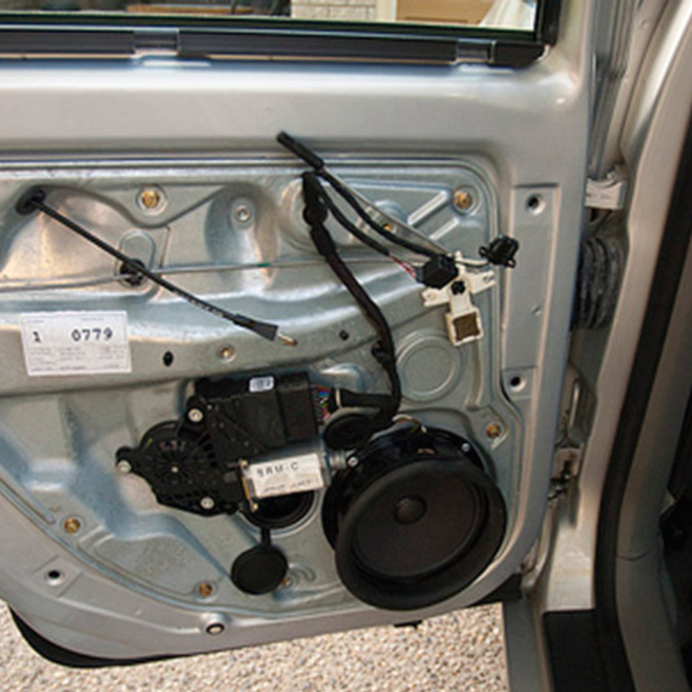 Car door interior panel removed, showing window motor, speaker, and wiring harnesses
