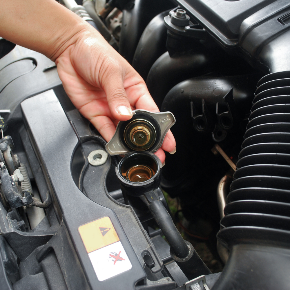 Hand holding a radiator cap over an open engine coolant reservoir in a car engine bay