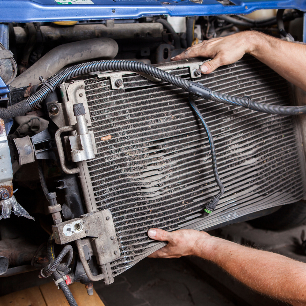 Hands removing a large car radiator in a blue vehicle engine bay