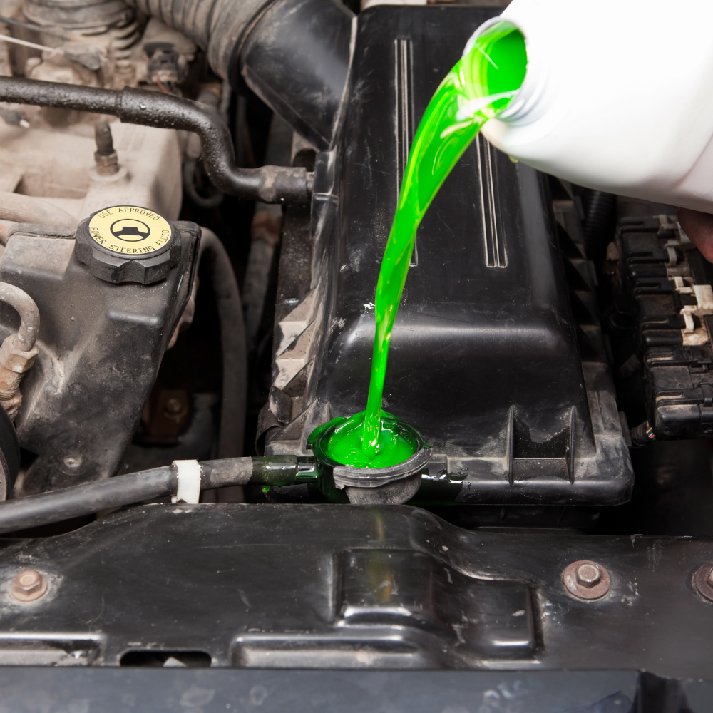 Bright green coolant being poured into a car engine radiator opening under the hood.