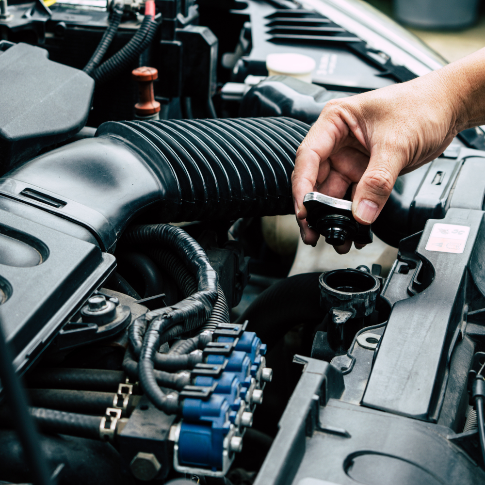 Hand holding a car engine cap beside the open hood and exposed components