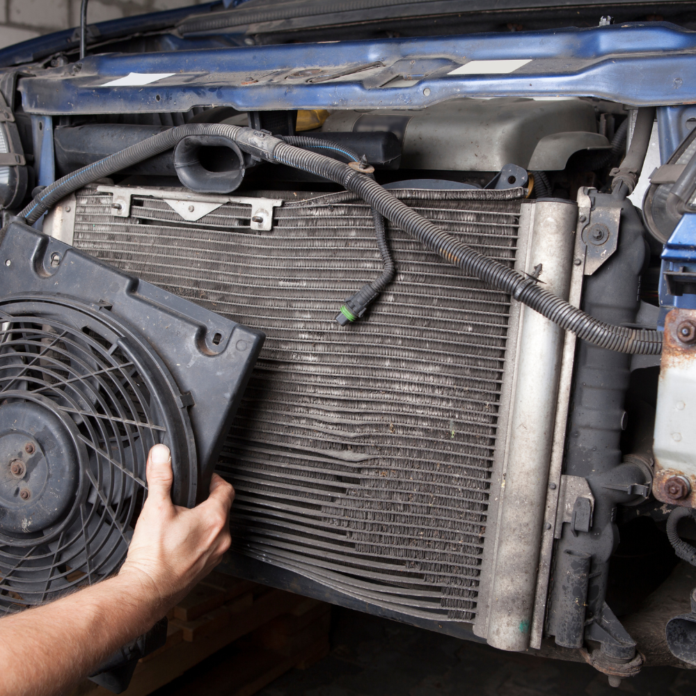 Hand holding a car radiator and fan assembly removed from the front end of a vehicle