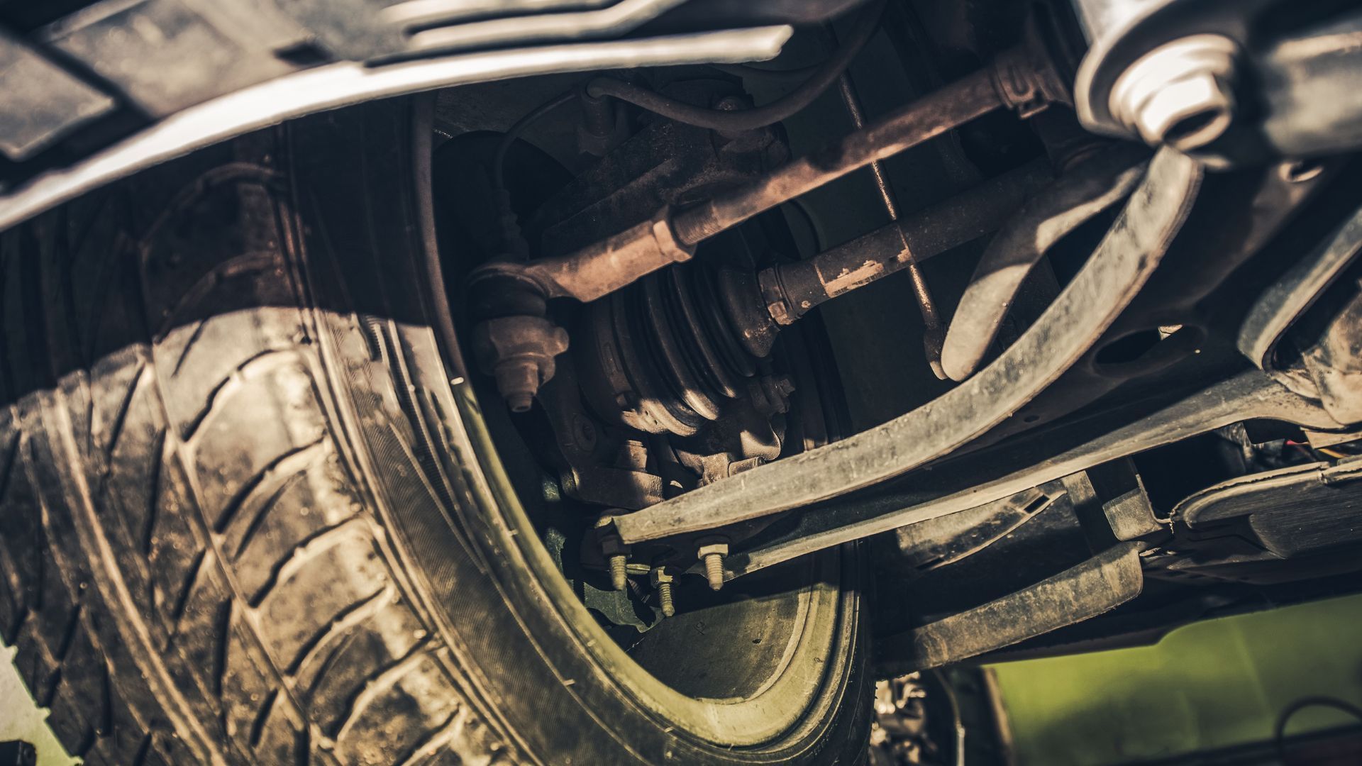 Close-up of a car’s front tire and suspension undercarriage, muddy and worn.