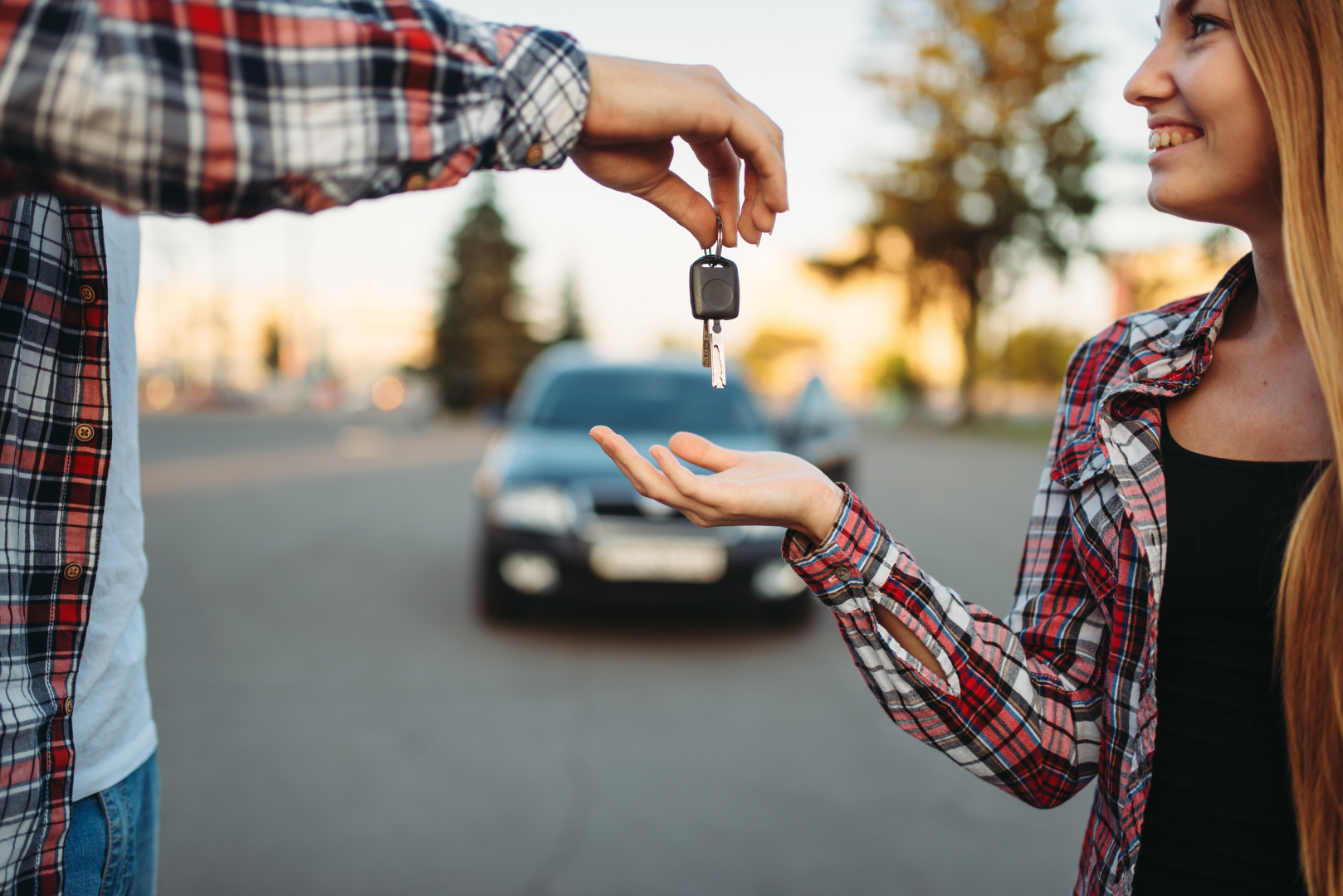 Person handing car keys to another person on a street with a car in the background