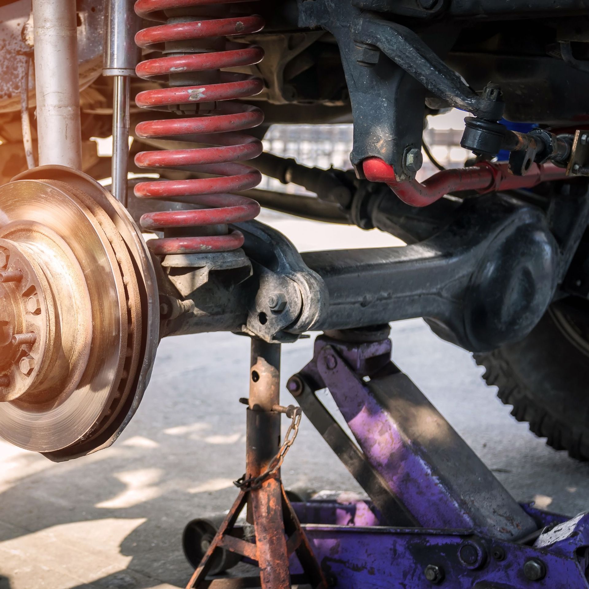 Car suspension with red coil spring and brake disc raised on a purple jack