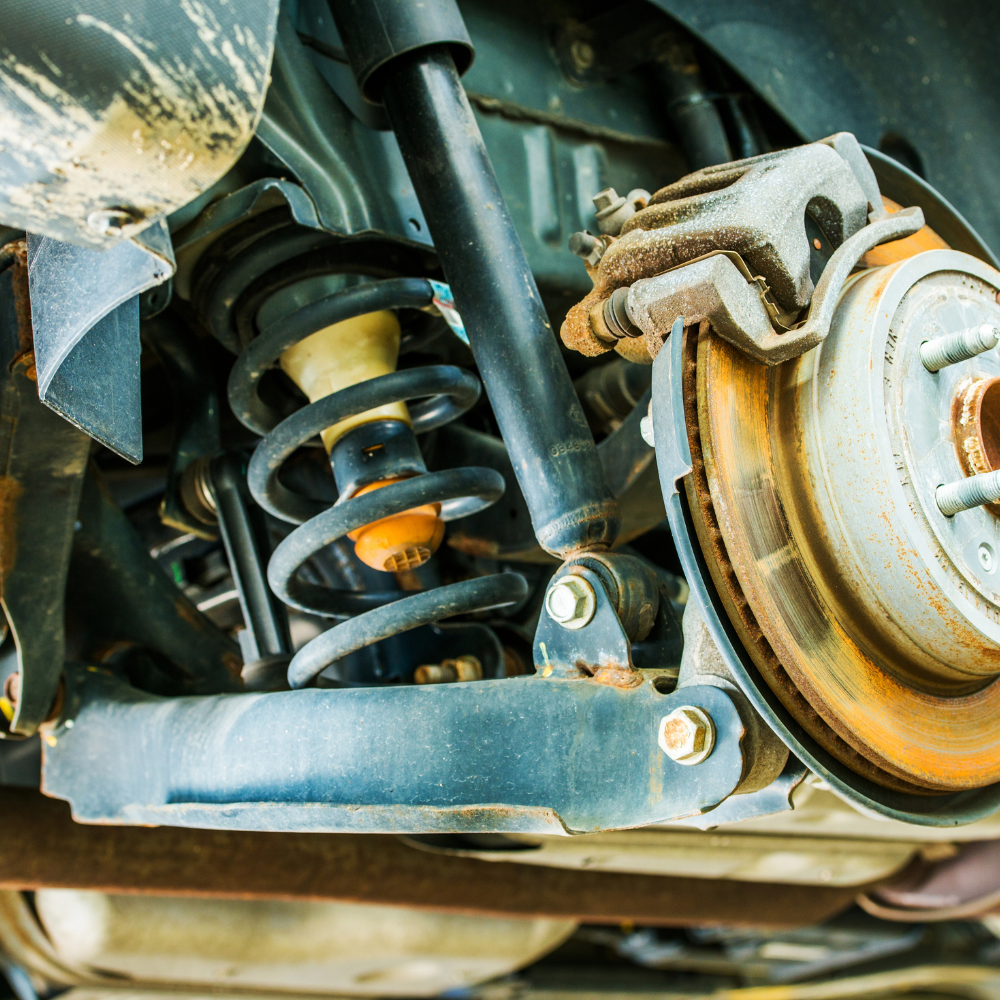 Close-up of a vehicle suspension with coil spring, shock absorber, and brake assembly in a garage setting
