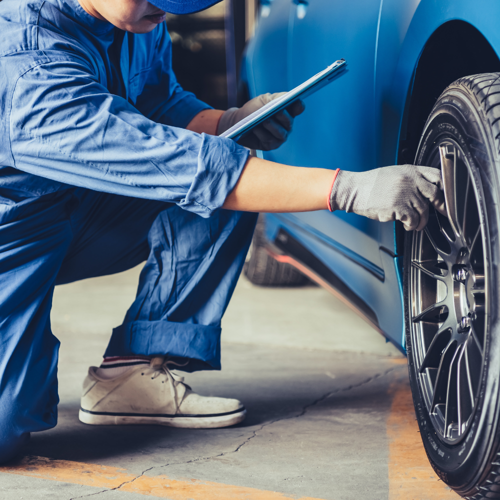 Mechanic in blue coveralls inspecting a car wheel with a tablet