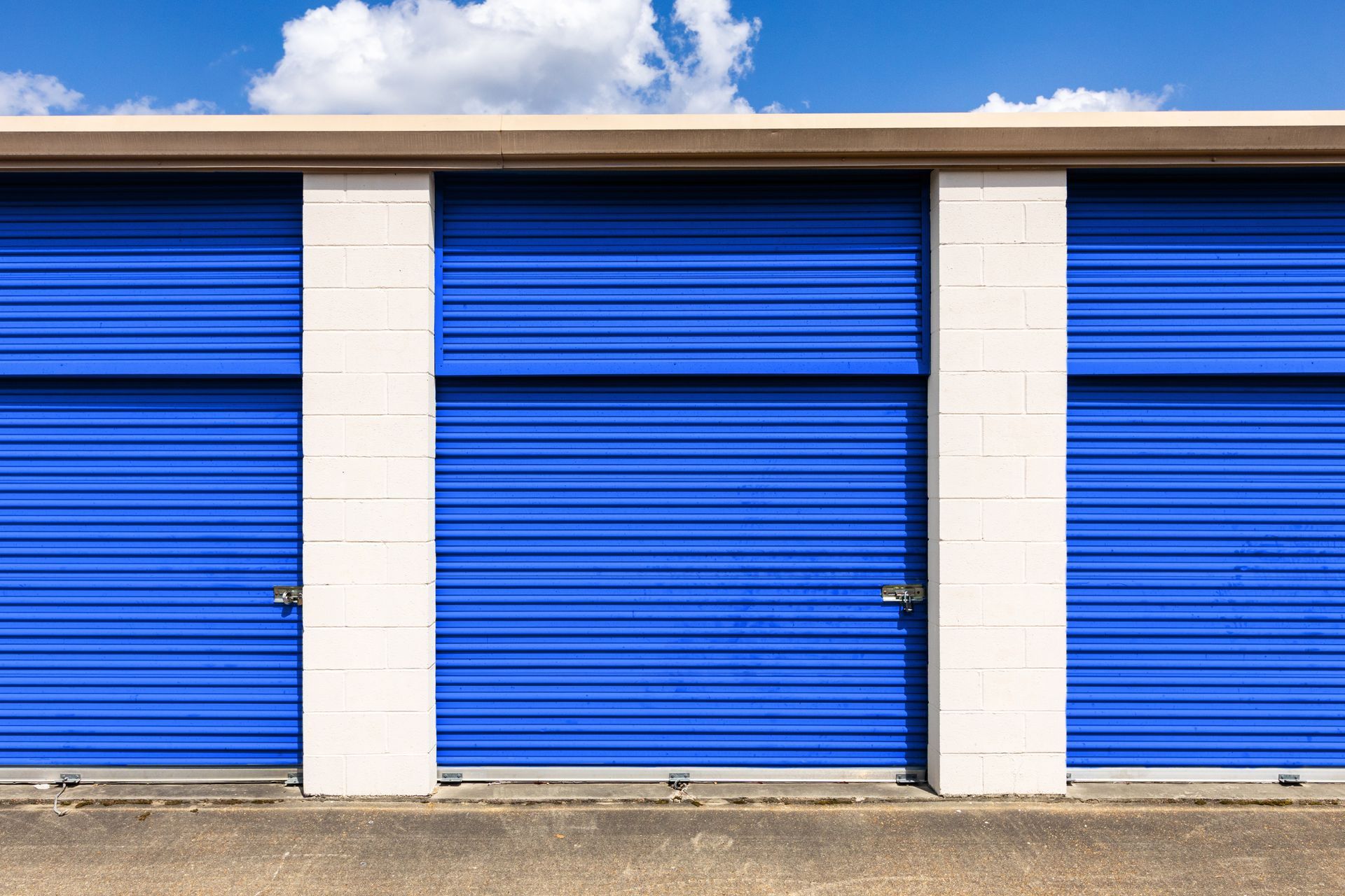Row of blue roll-up storage unit doors with white block dividers under a blue sky.