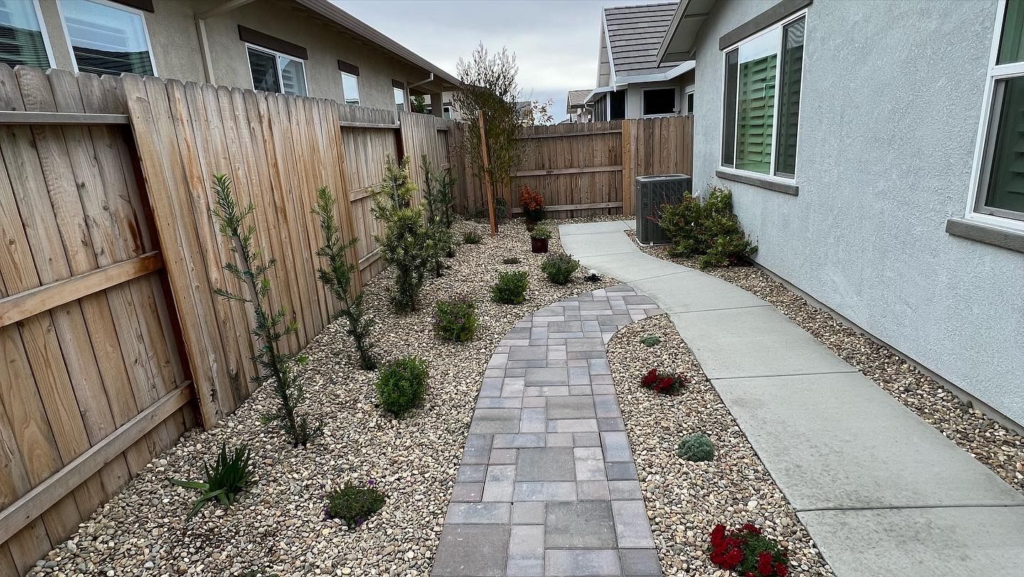 A brick walkway leading to a house with a wooden fence.