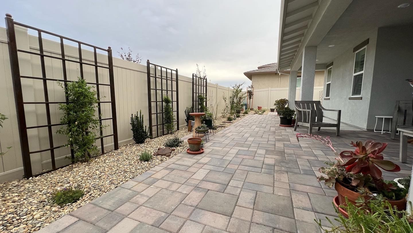 A brick walkway leading to a house with a fence and a bench.