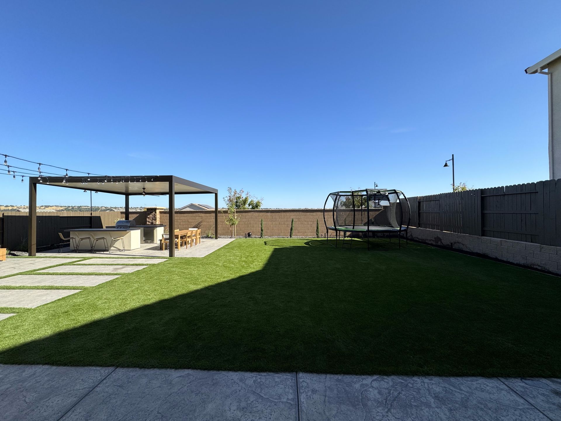 A large lawn with a pergola and a fence in the backyard of a house.
