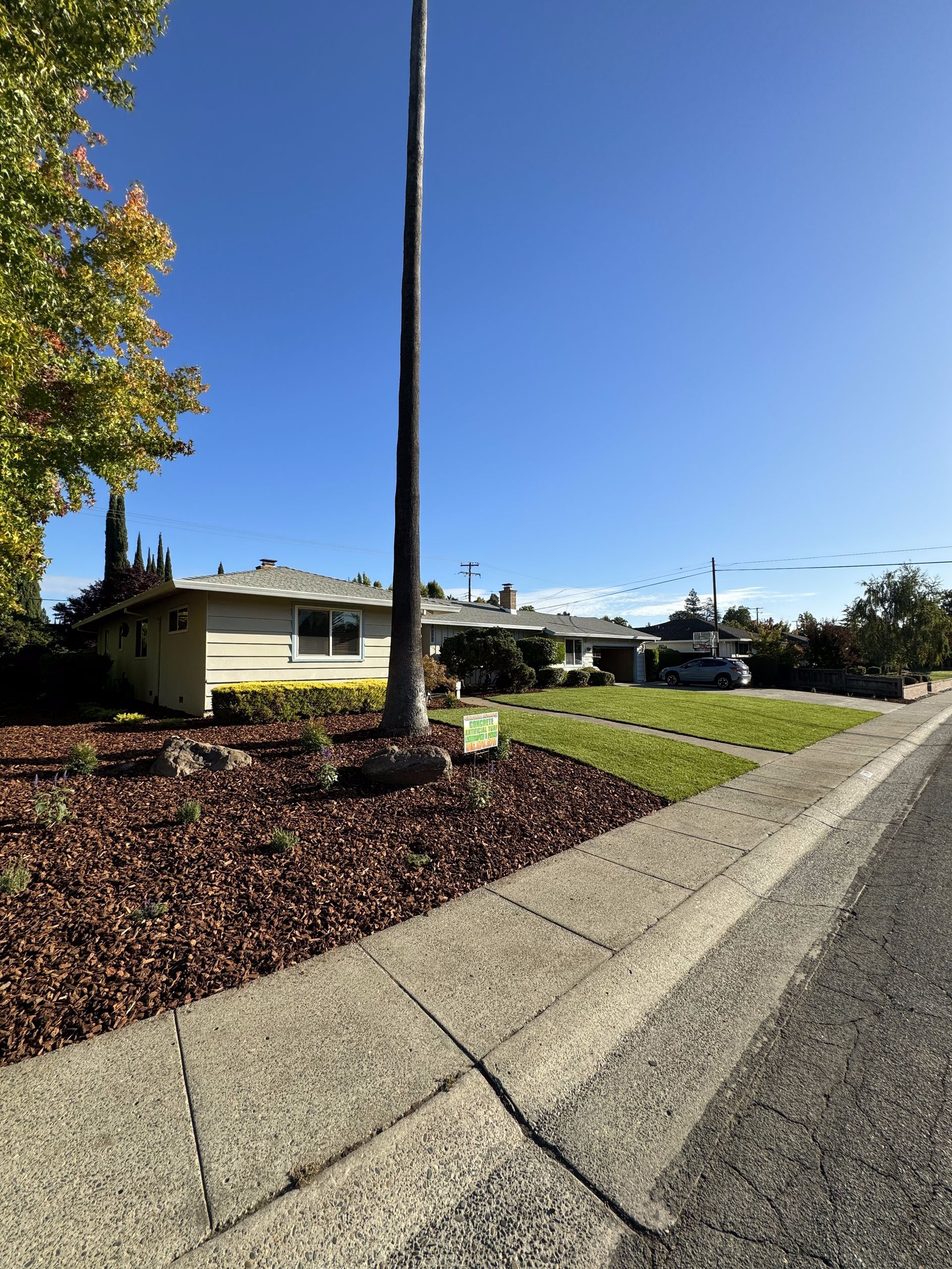A house is sitting on the side of the road next to a sidewalk.