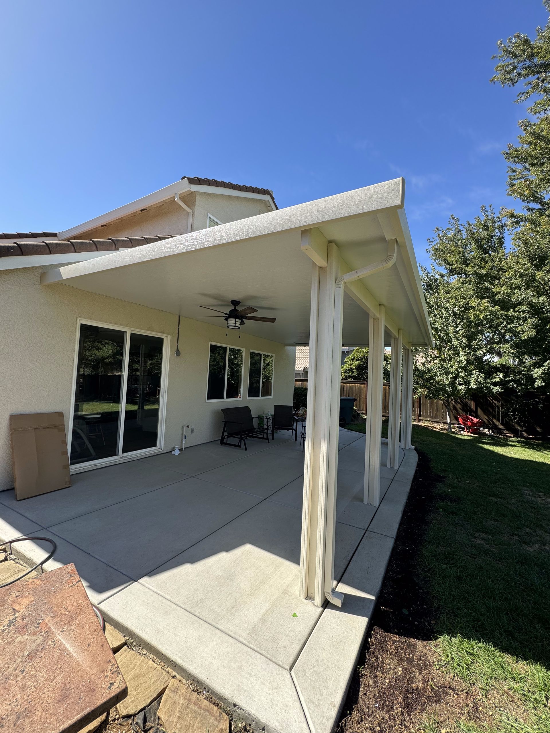 There is a patio with a ceiling fan and a table in the backyard of a house.