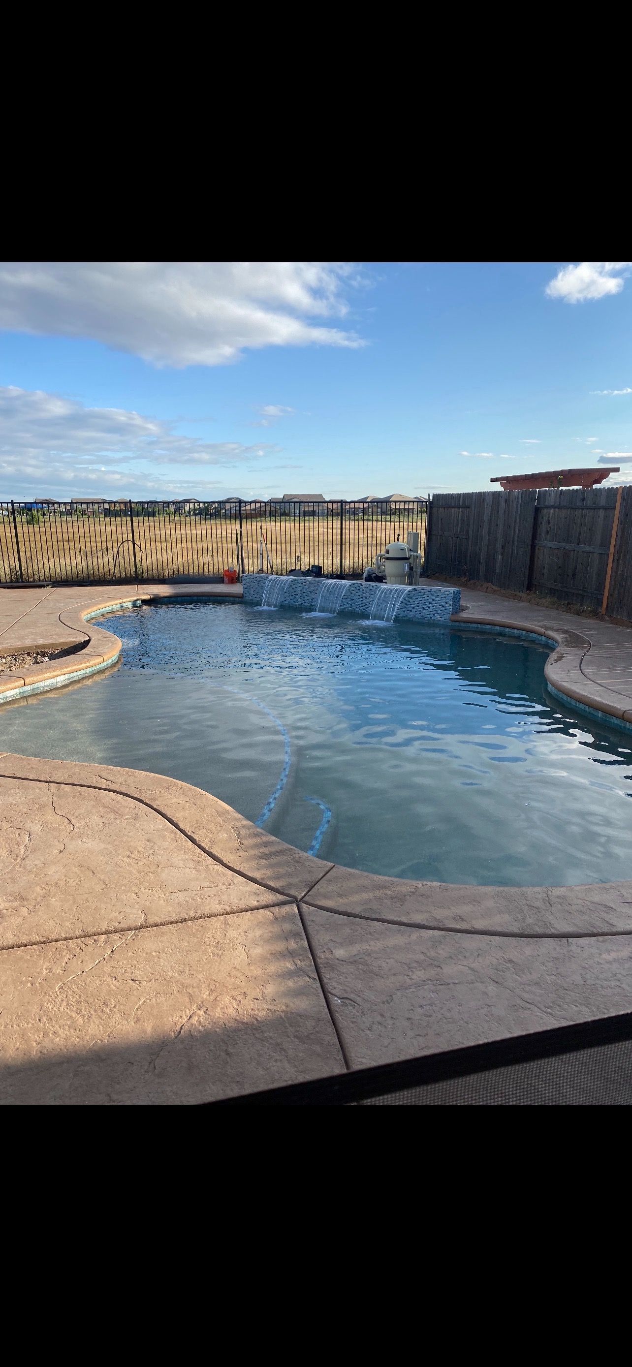 A large swimming pool with a fence around it and a blue sky in the background.