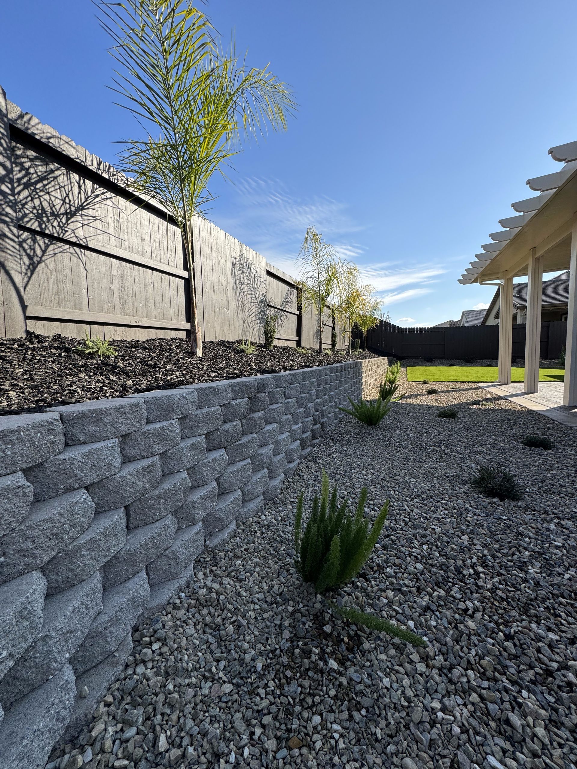 A gravel yard with a fence and a pergola in the background.
