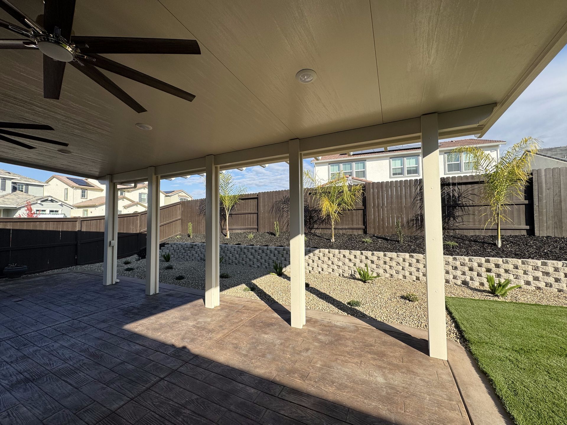 A patio with a ceiling fan and a fence in the background.