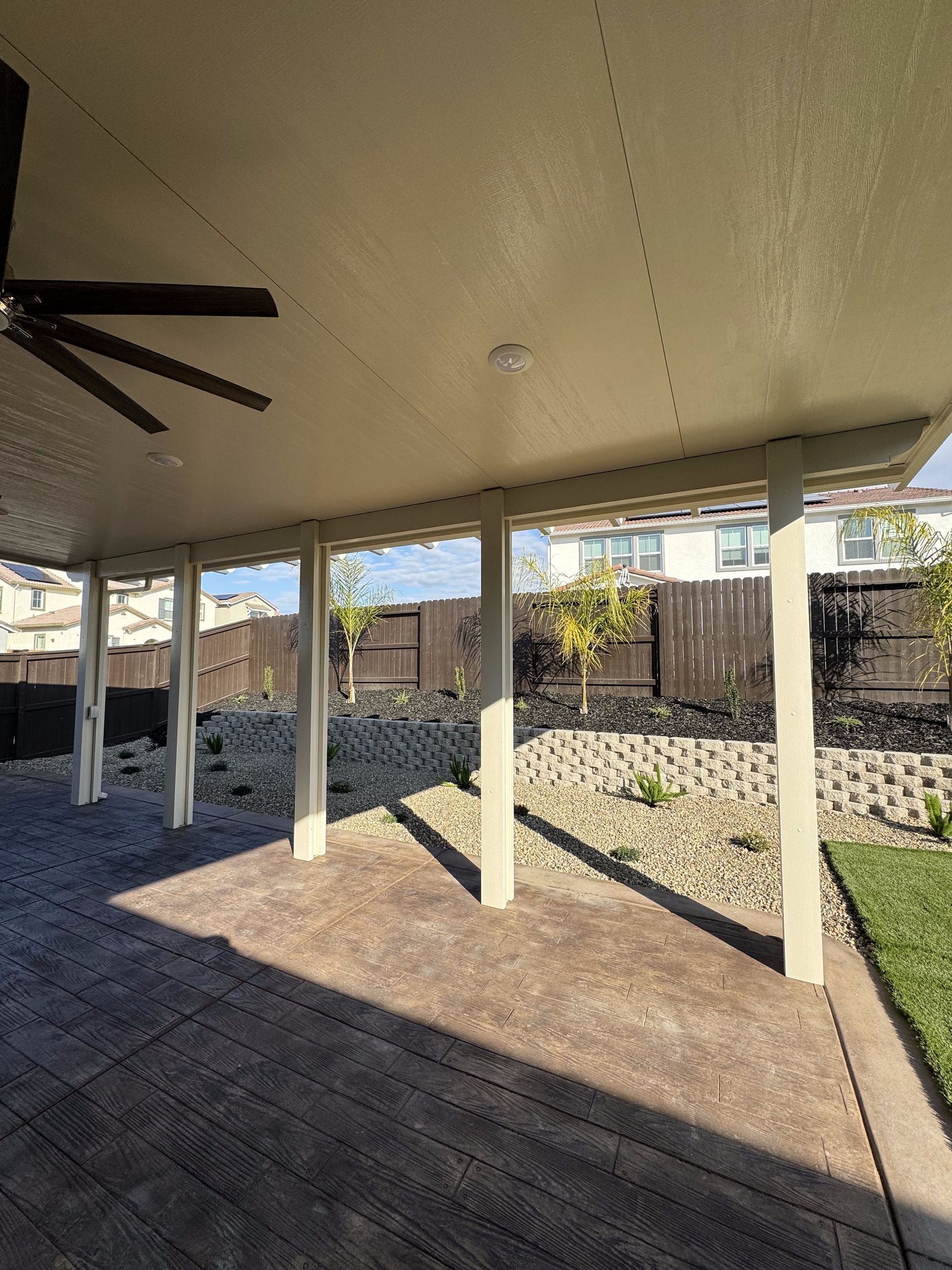 A covered patio with a ceiling fan and a fence in the background.