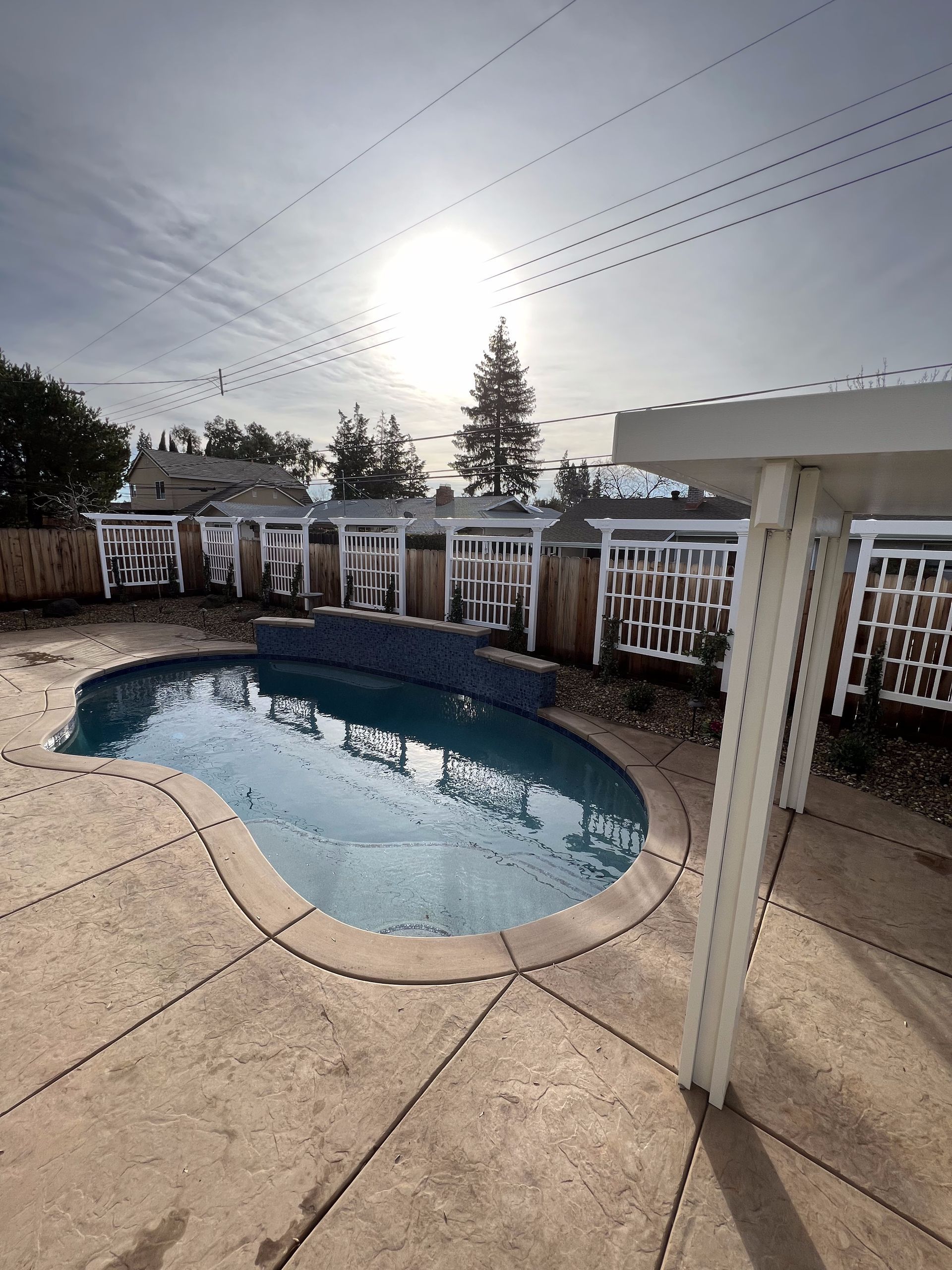 A large swimming pool is surrounded by a fence and a patio.