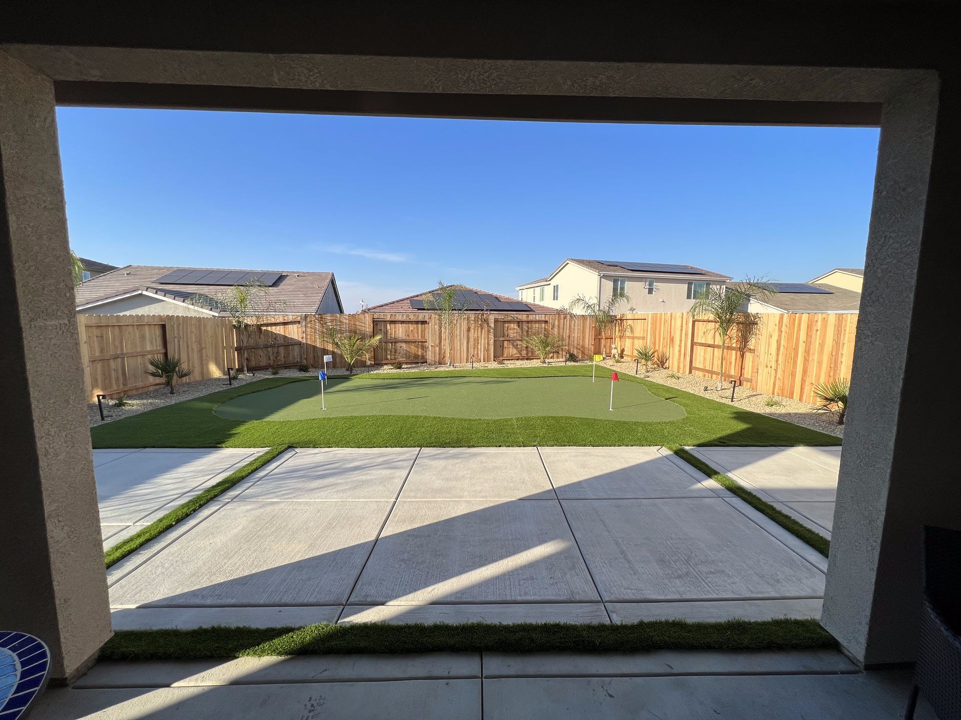 A view of a backyard with a putting green and a fence.