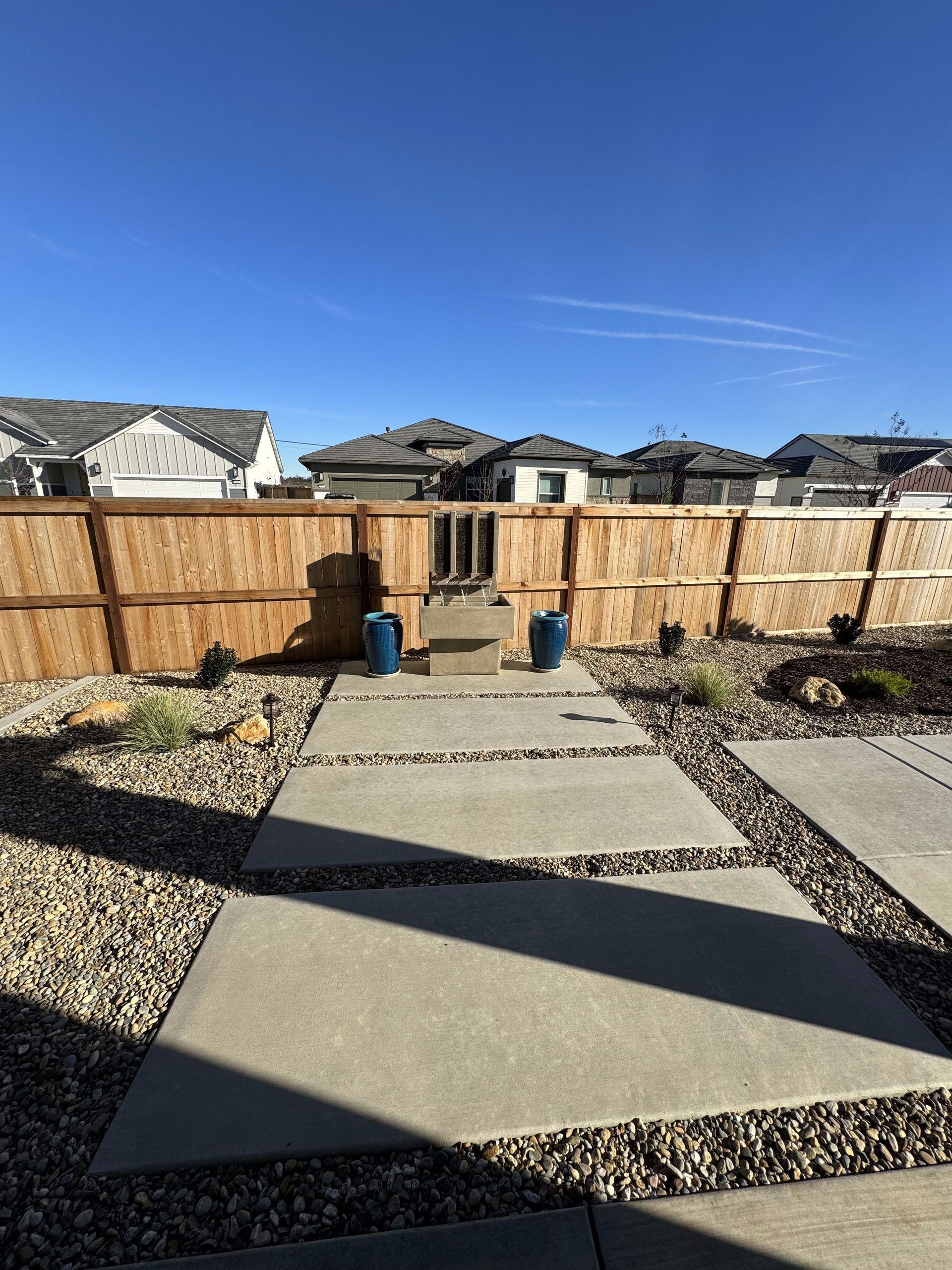 A wooden fence surrounds a concrete walkway in a backyard.