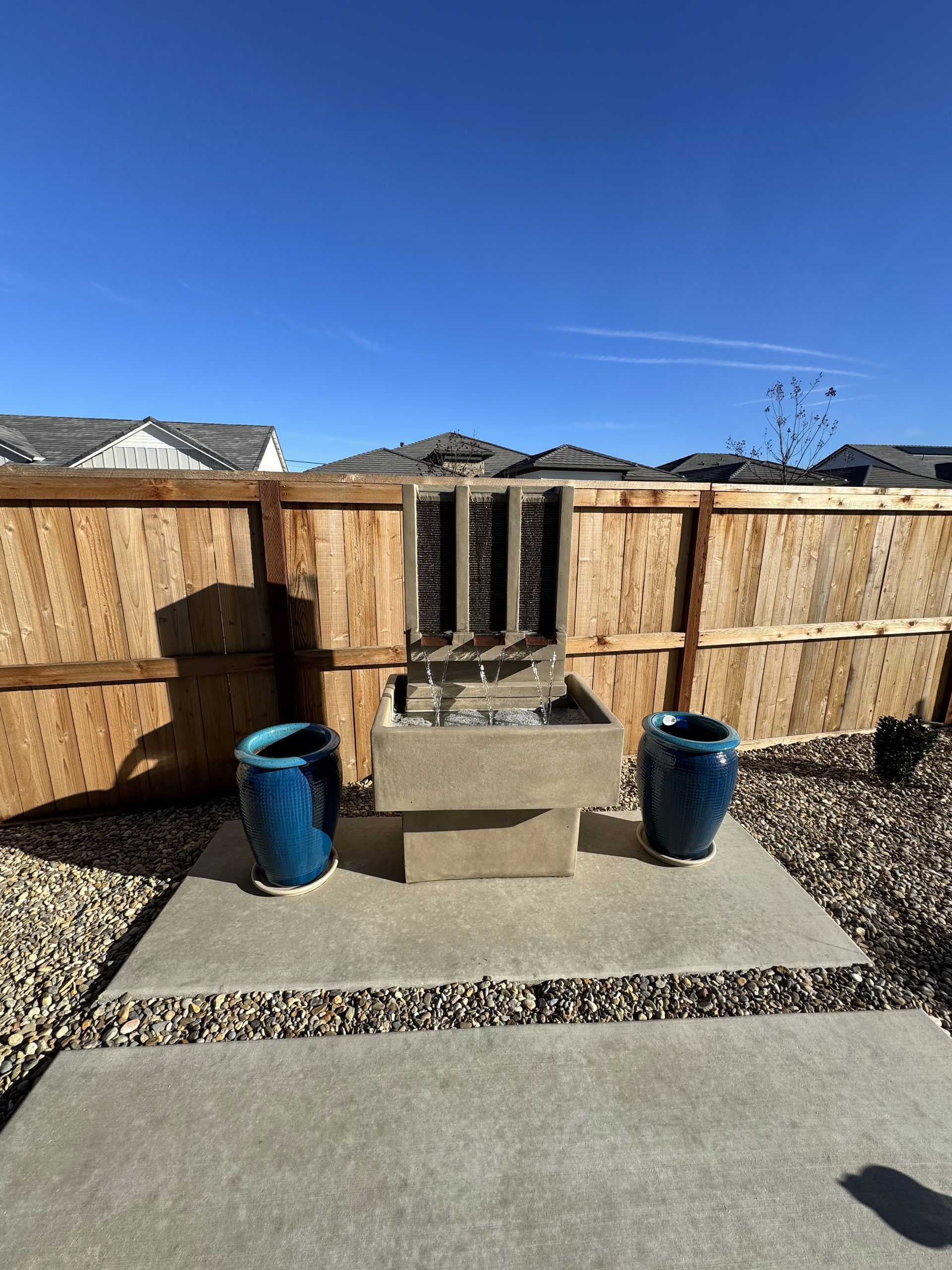 A fountain with two blue pots in front of a wooden fence.
