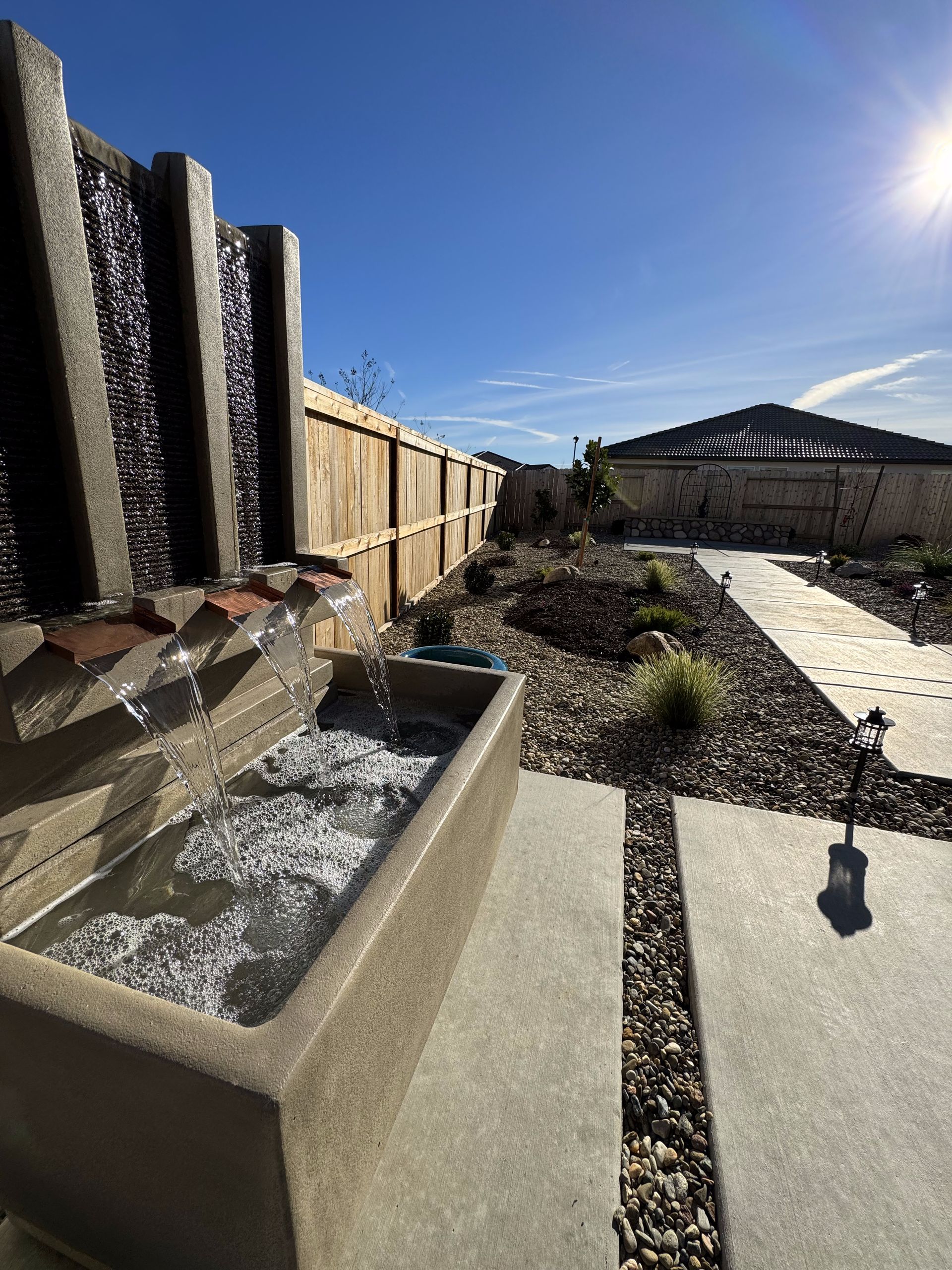A water fountain in a backyard with a wooden fence in the background