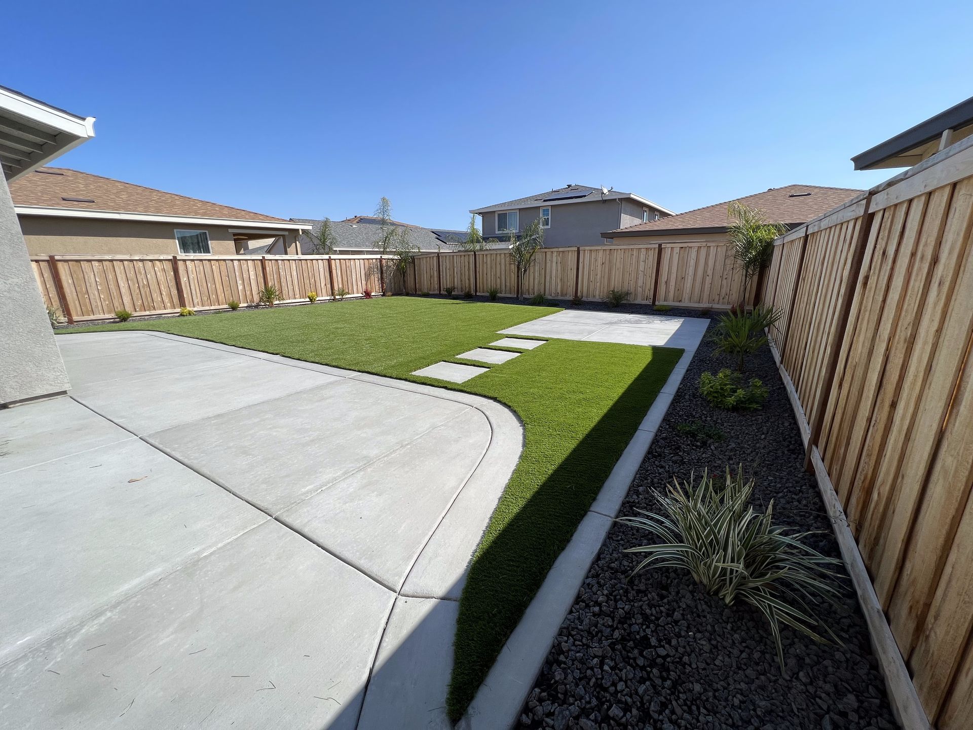A backyard with a wooden fence and a concrete walkway