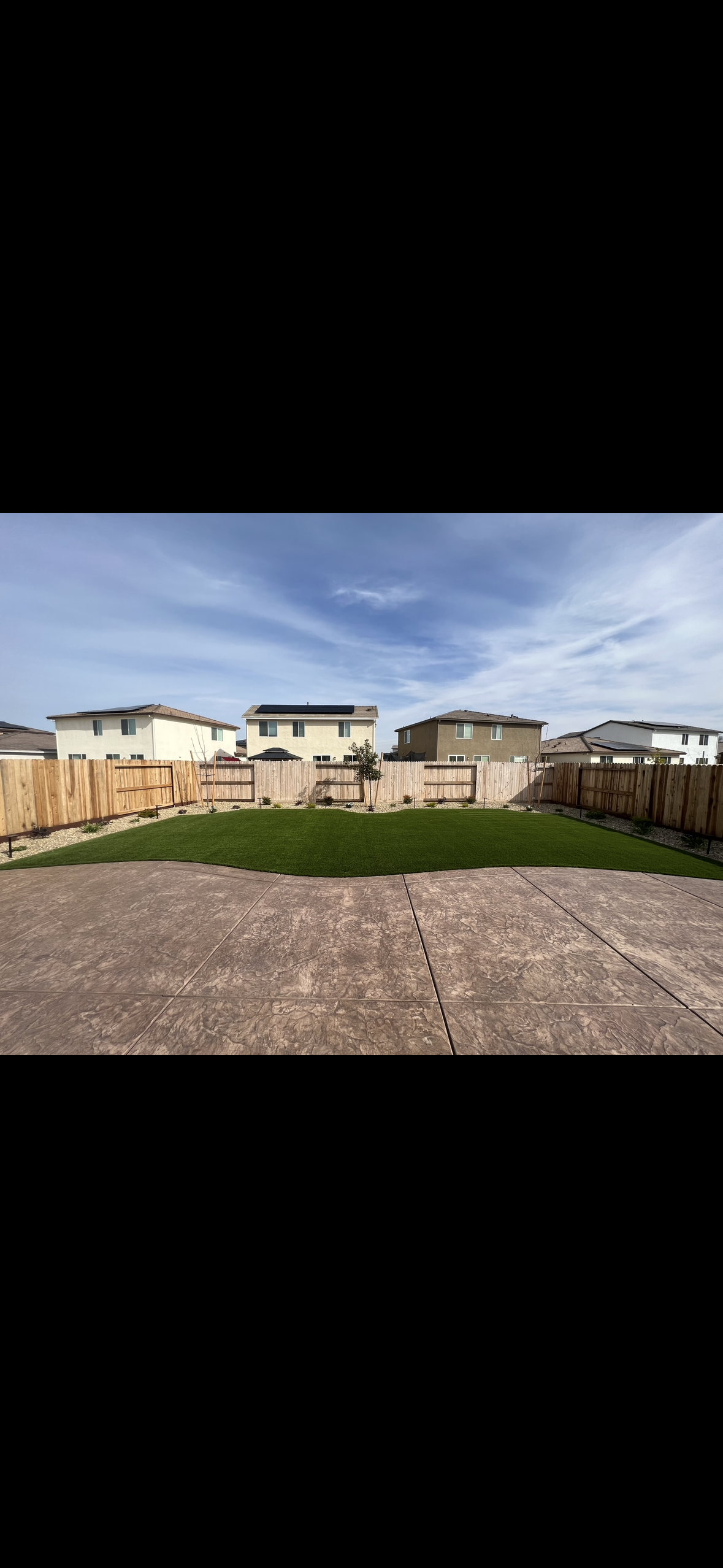 A large lawn with a fence in the background and houses in the background.