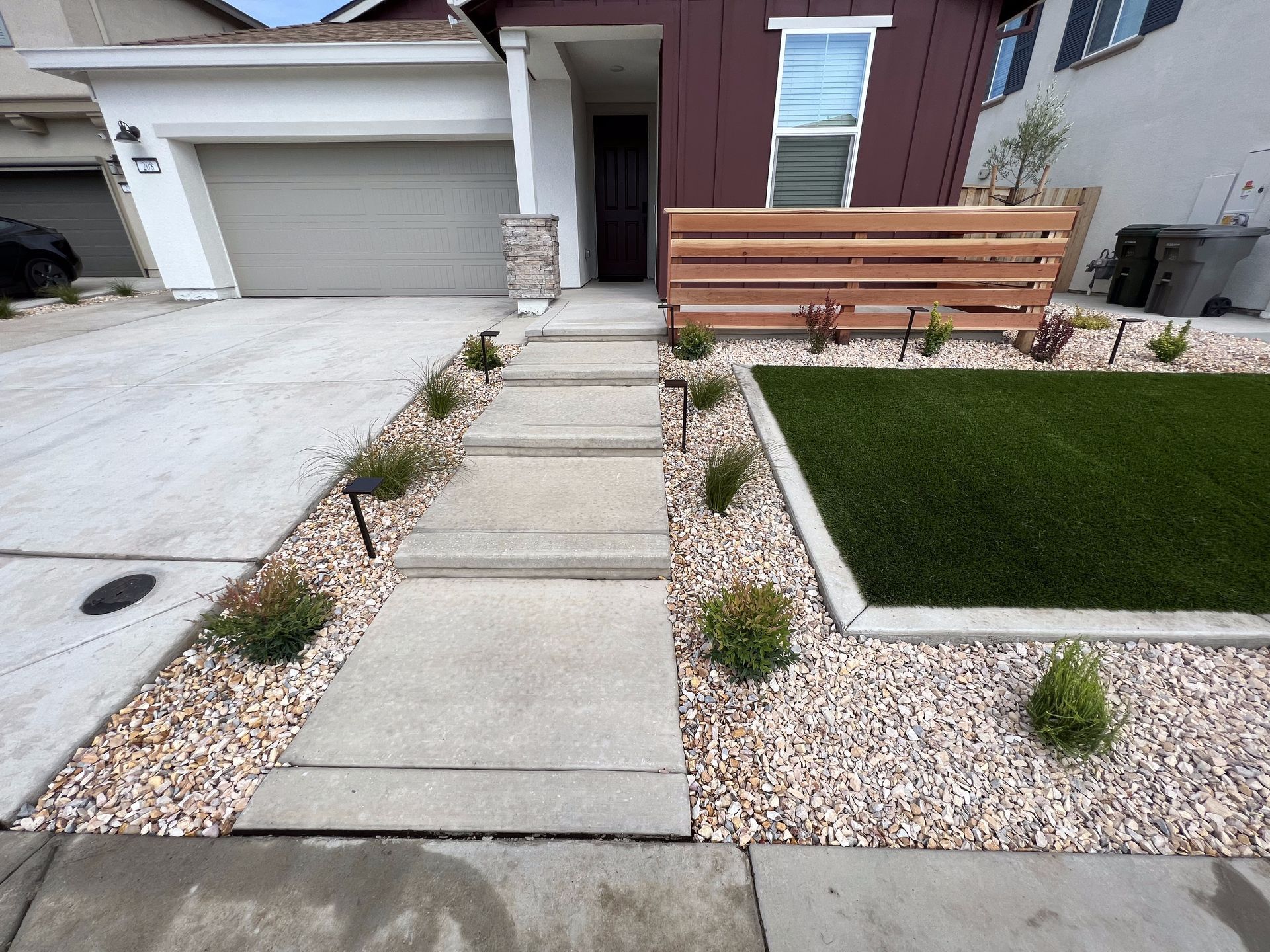 A concrete walkway leading to a house with gravel and grass