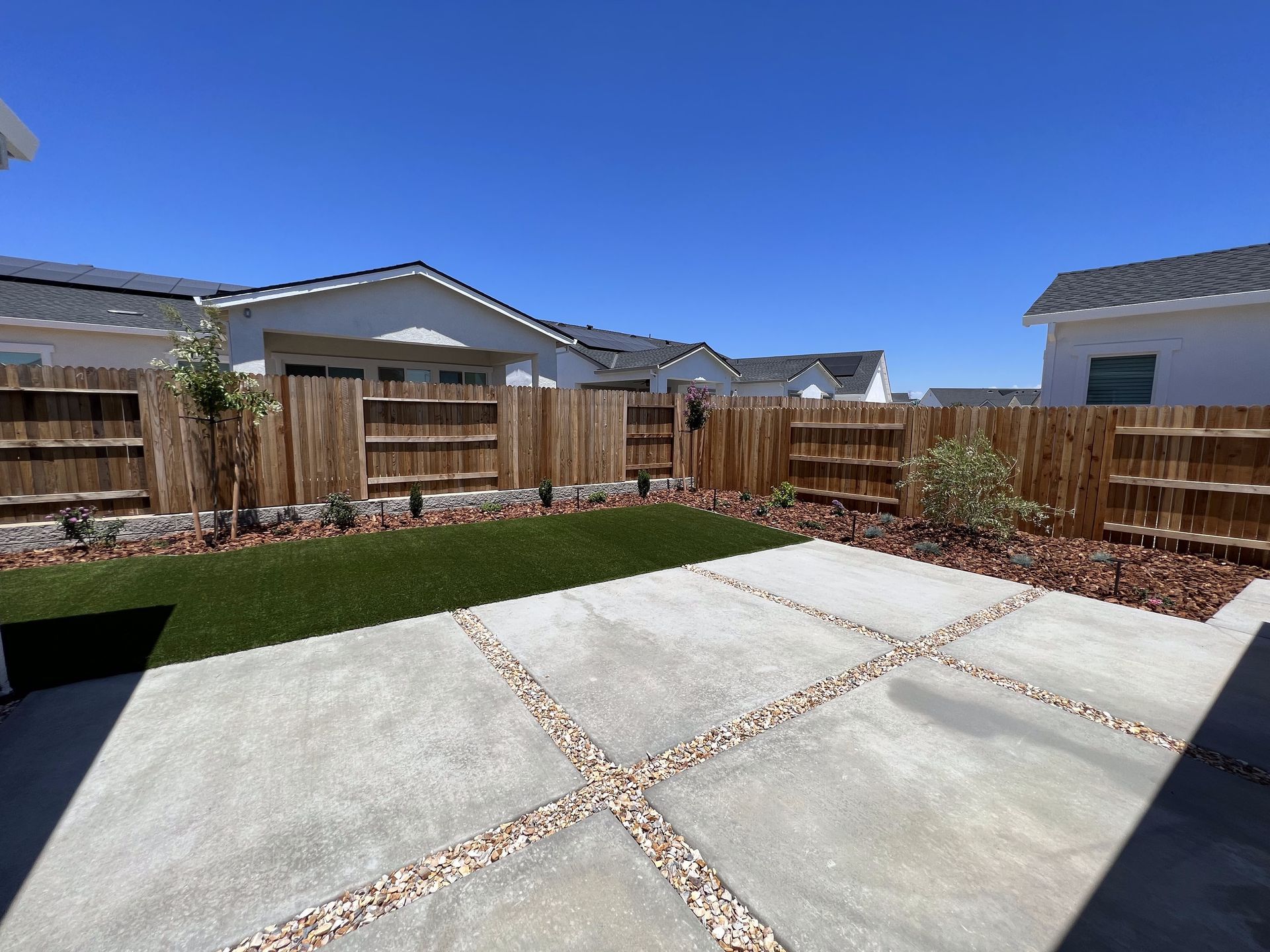 A backyard with a wooden fence and a concrete walkway