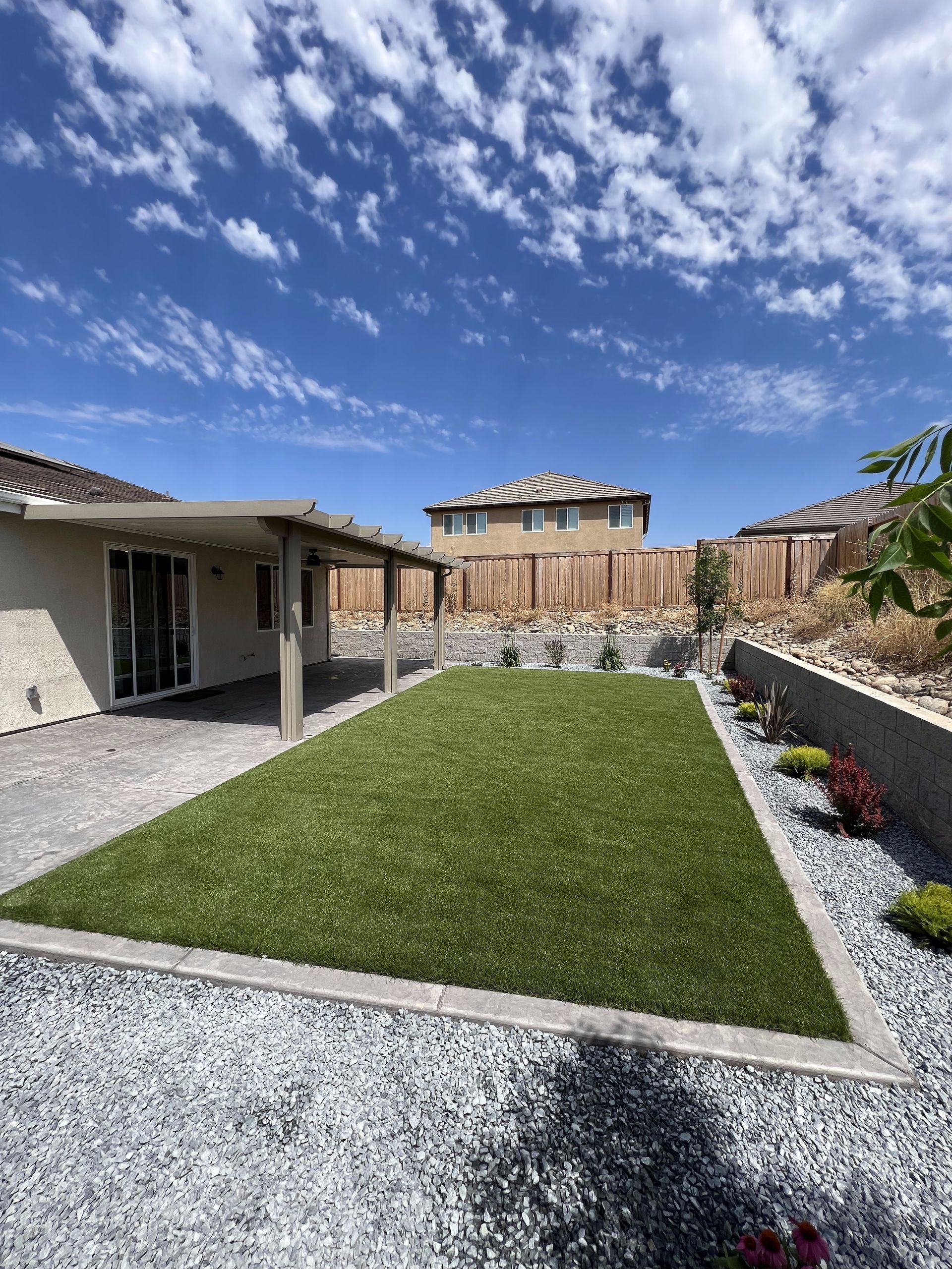 A large lawn in front of a house with a covered patio.