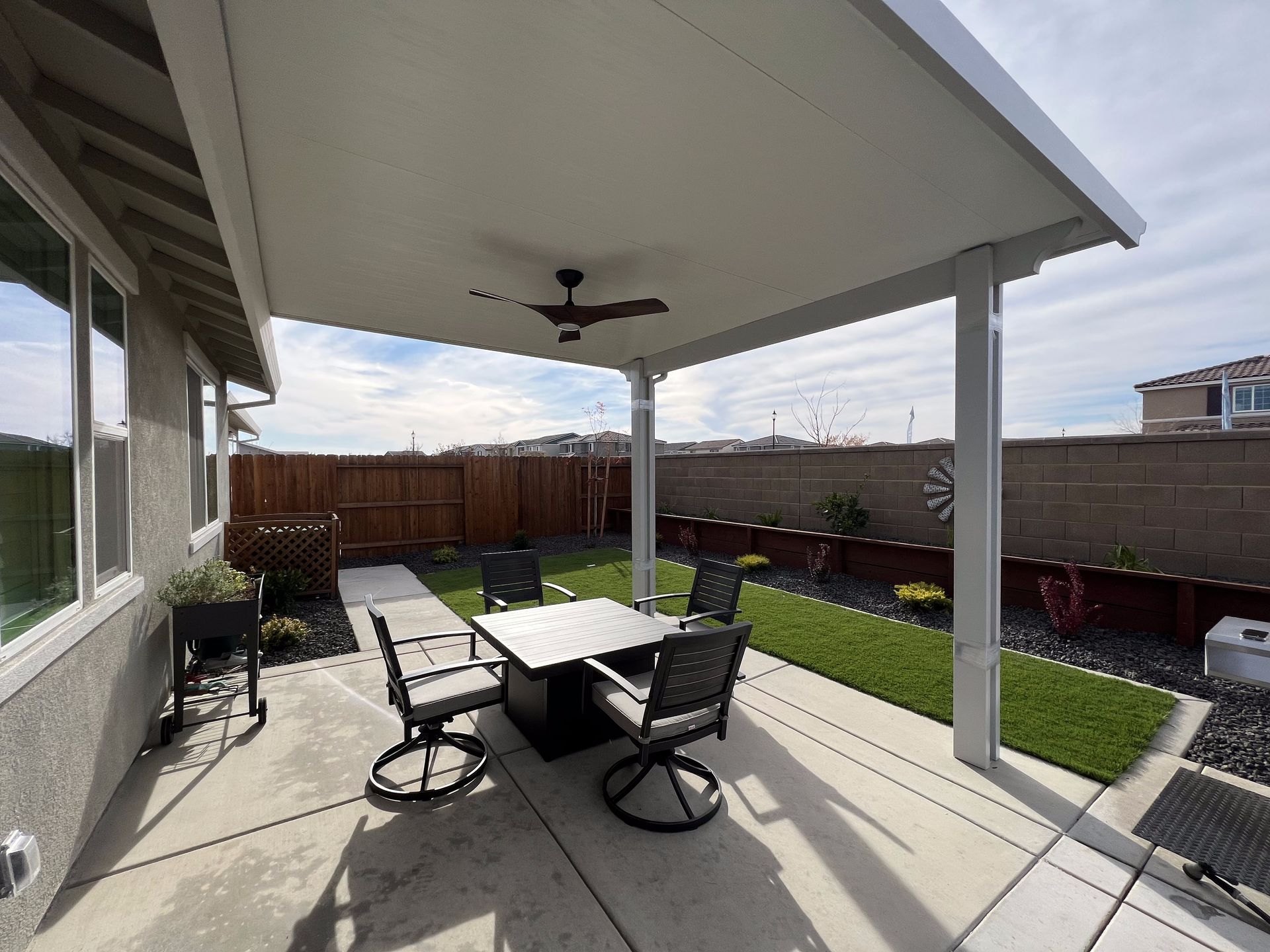 A patio with a table and chairs under a roof with a ceiling fan.