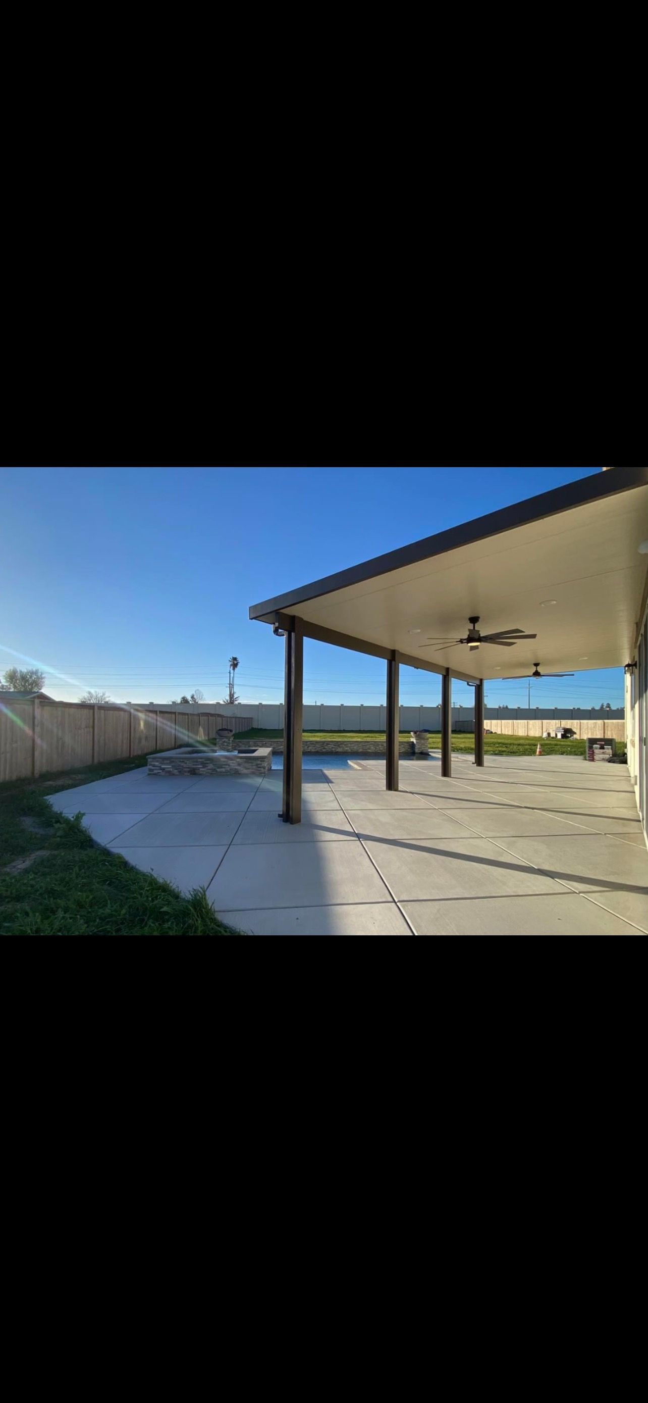 A large covered patio with a ceiling fan in the backyard of a house.