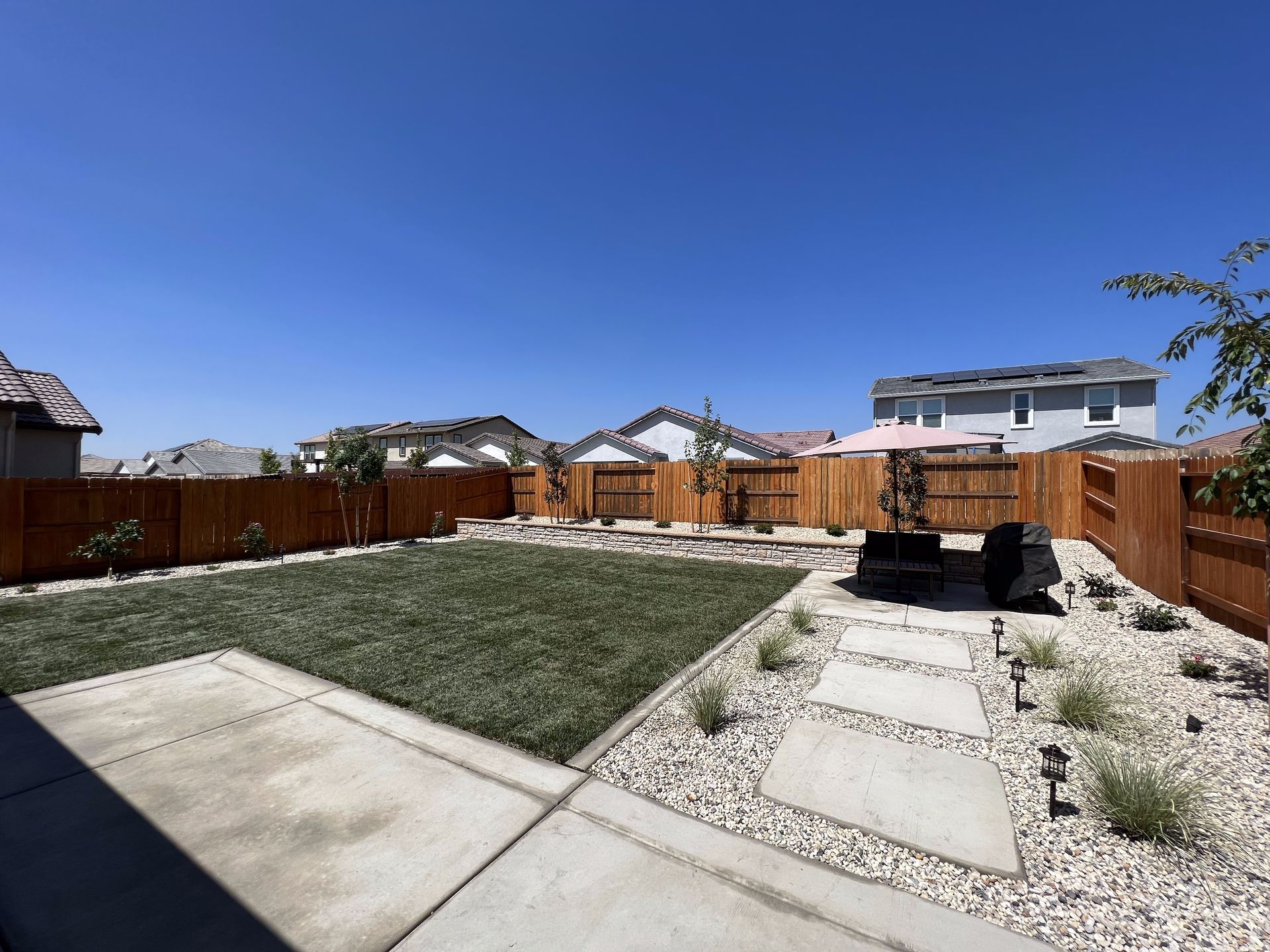 A backyard with a concrete walkway and a wooden fence