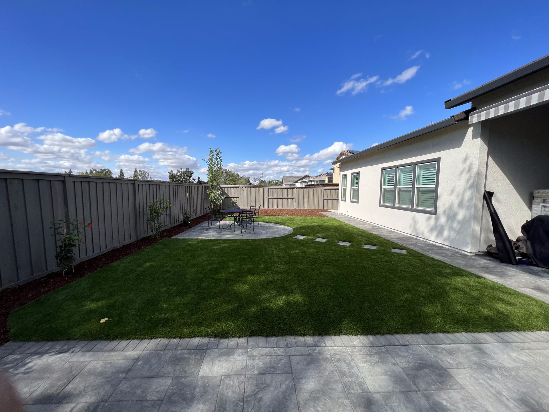 A backyard of a house with a fence and a lush green lawn.