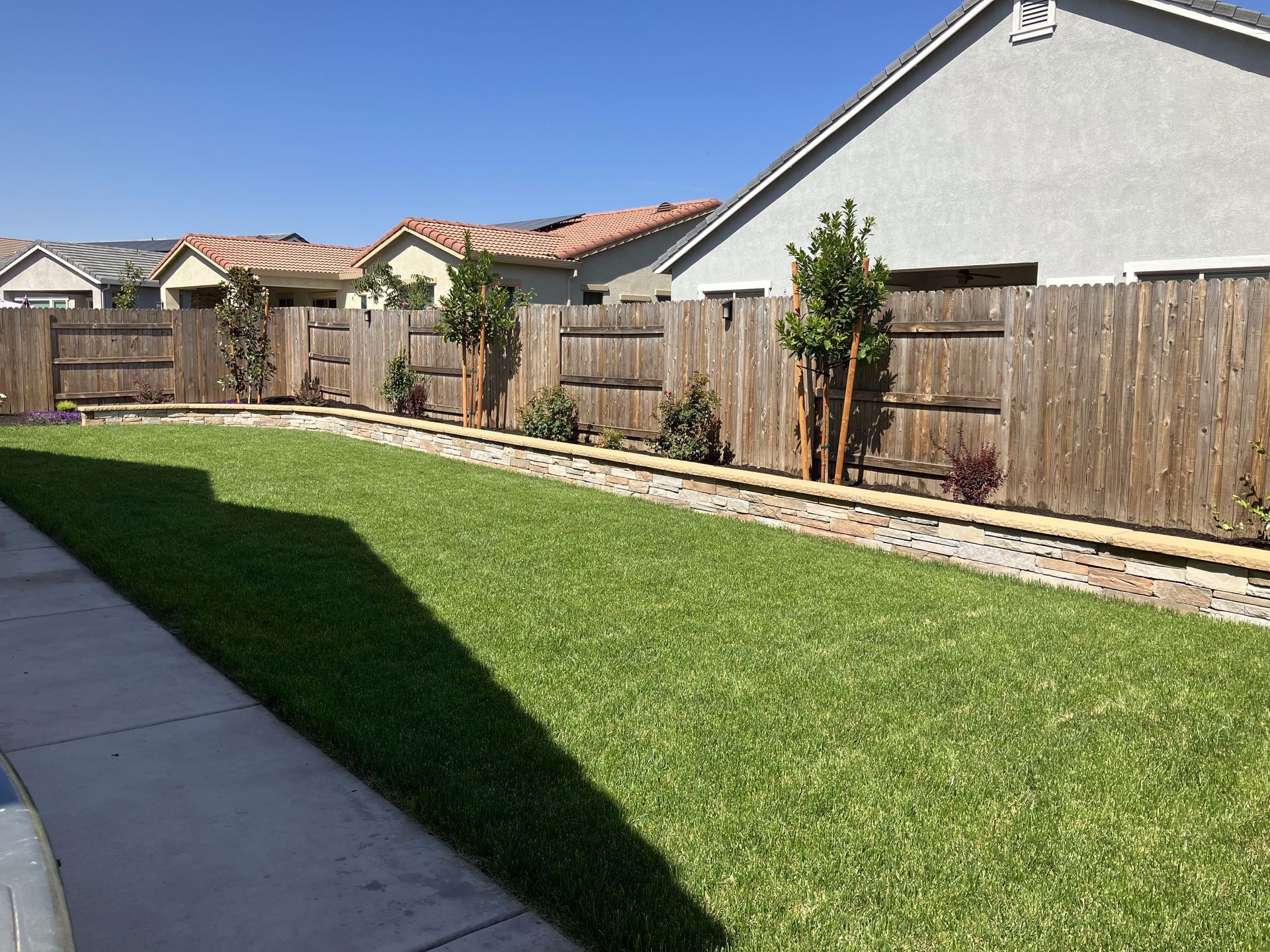 A wooden fence surrounds a lush green lawn in front of a house.