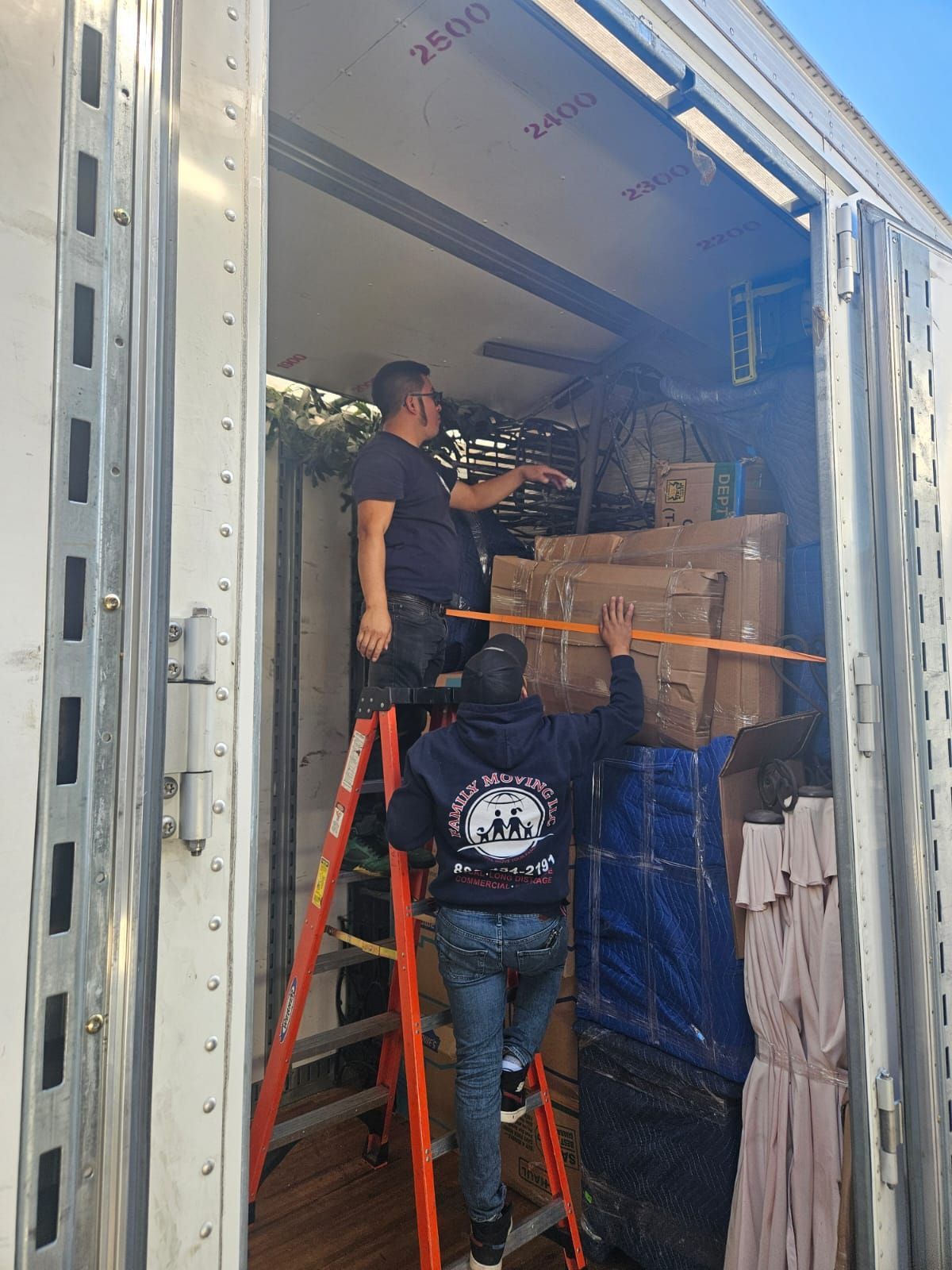 A man on a ladder is measuring a box in a truck.