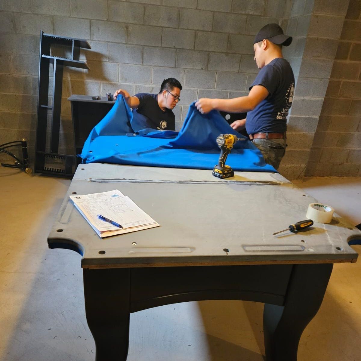 Two men are working on a pool table in a basement