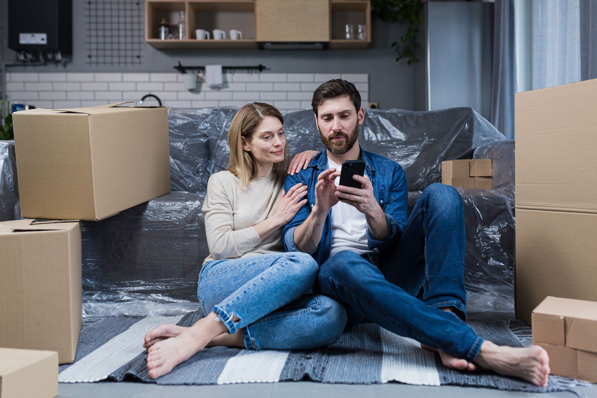 A man and a woman are sitting on the floor looking at a cell phone.