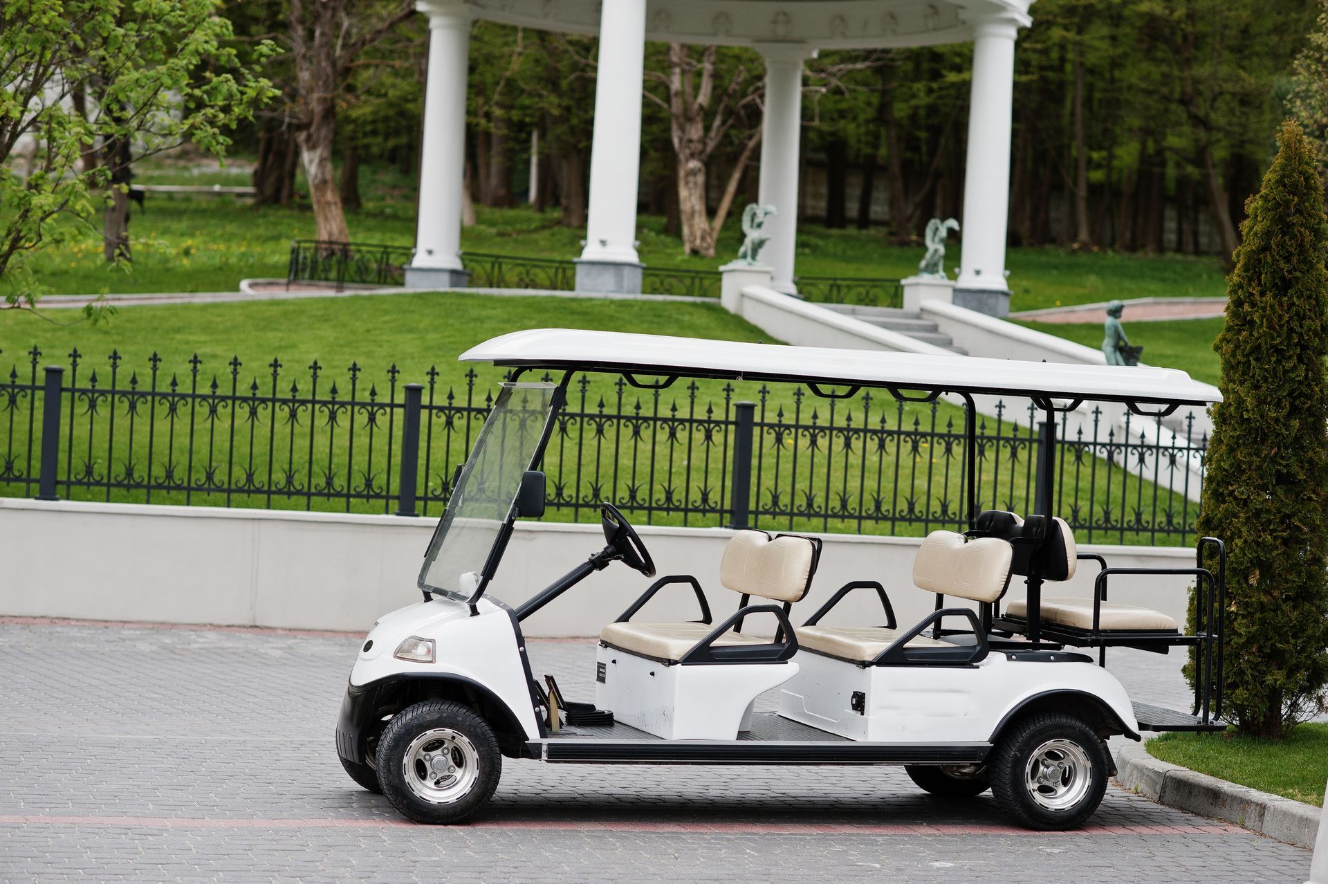 A white golf cart is parked in front of a gazebo in a park.