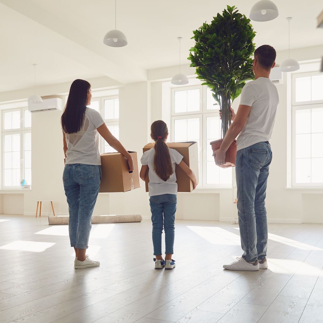 A family is moving into a new house and holding boxes and a potted plant.