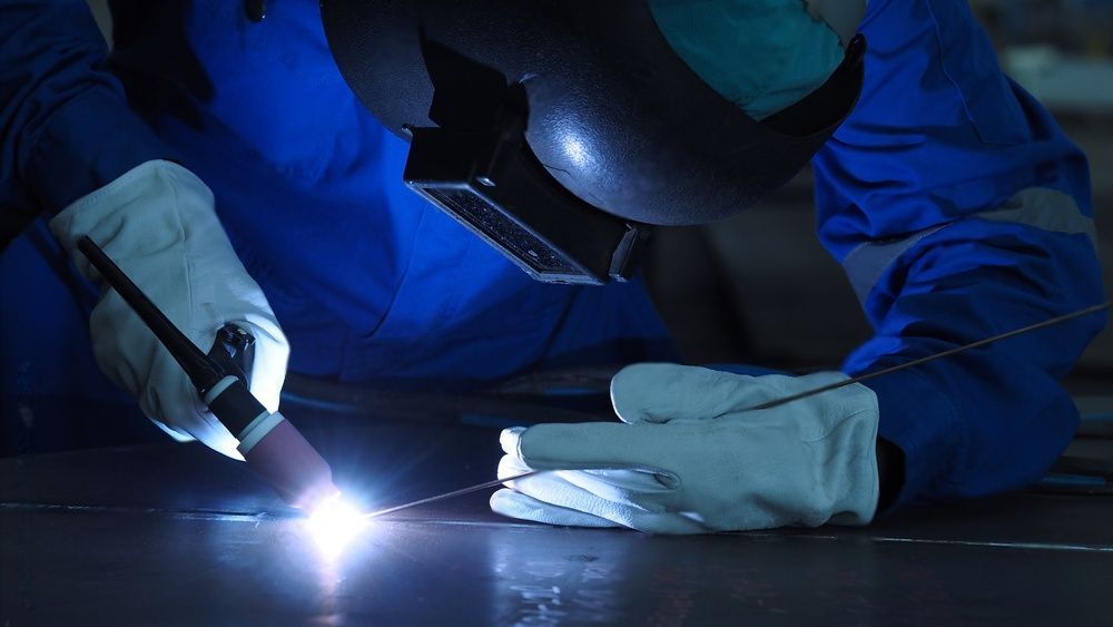 Een man met een helm en handschoenen is bezig met het lassen van een stuk metaal.