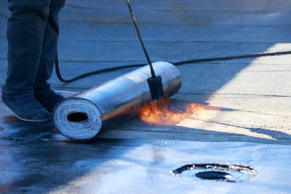 Een persoon rolt een rol dakbedekkingsmateriaal op een dak met een brander.